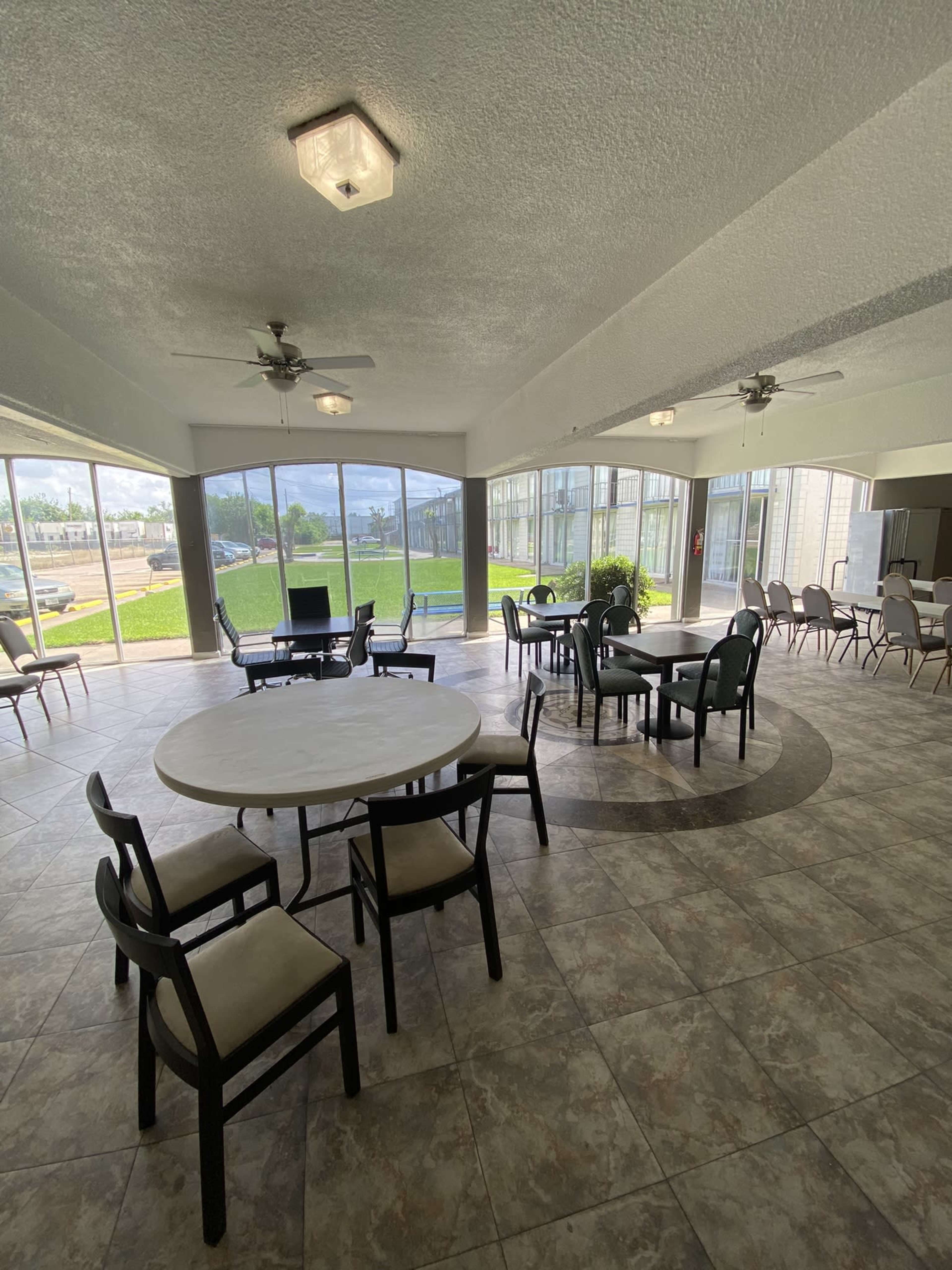 A spacious indoor seating area with tables and chairs, featuring large windows that provide a view of the outdoors.