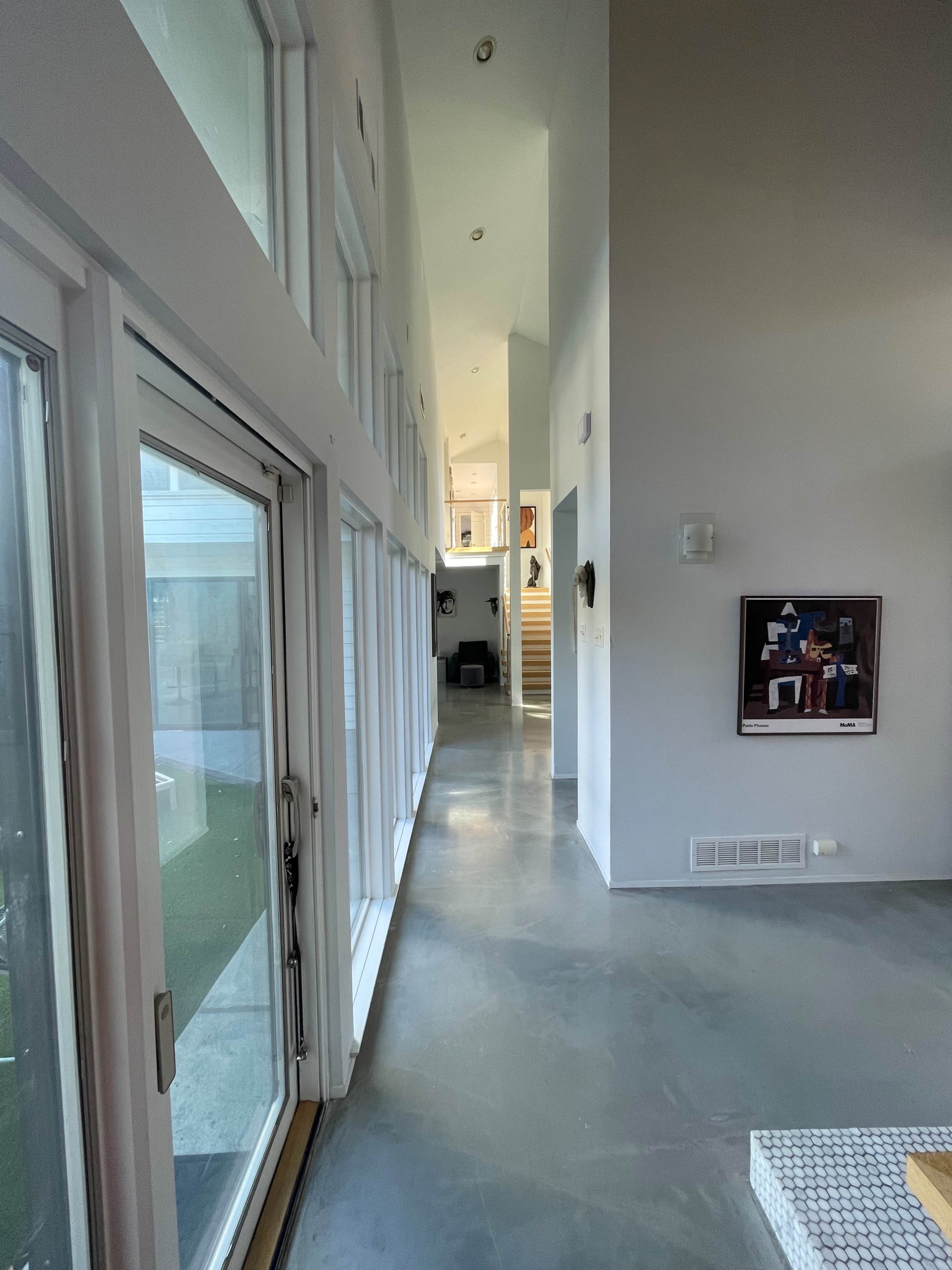 A long corridor with large windows, smooth concrete flooring, and a staircase at the end.