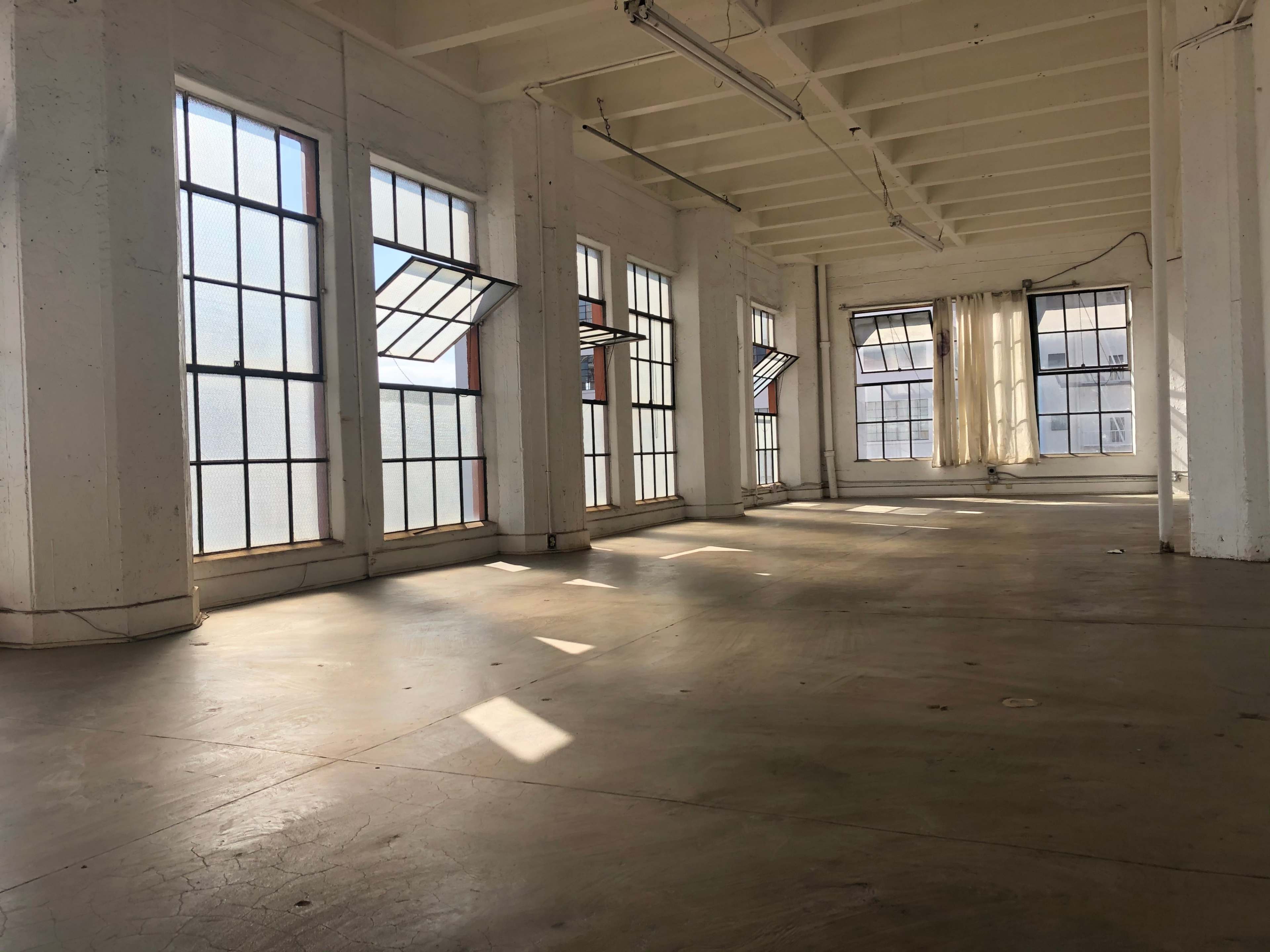 An empty, well-lit industrial space with large windows casting shadows on the concrete floor.