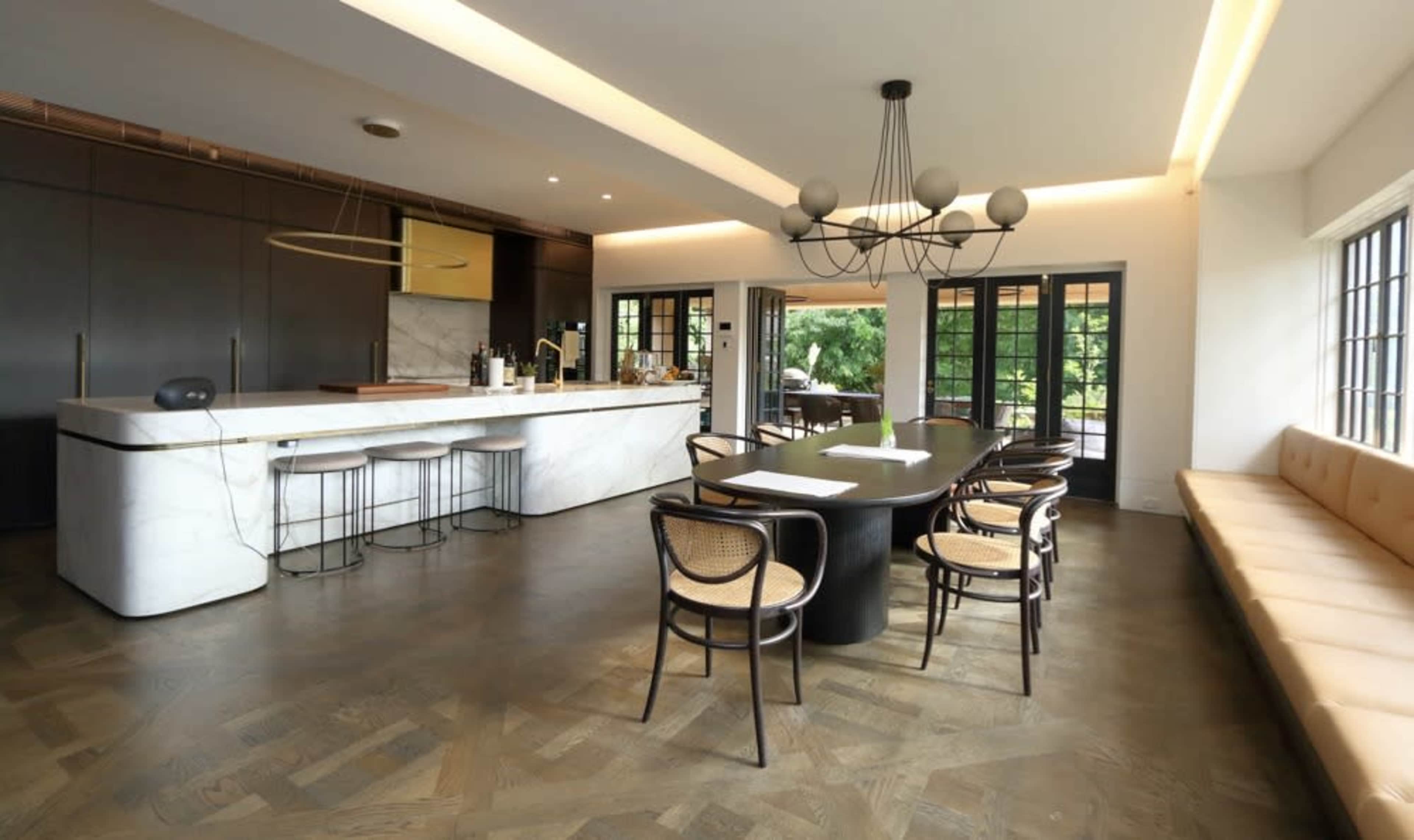 The image shows a modern kitchen and dining area with a white marble island, wooden dining table, and an arrangement of seating along the walls.