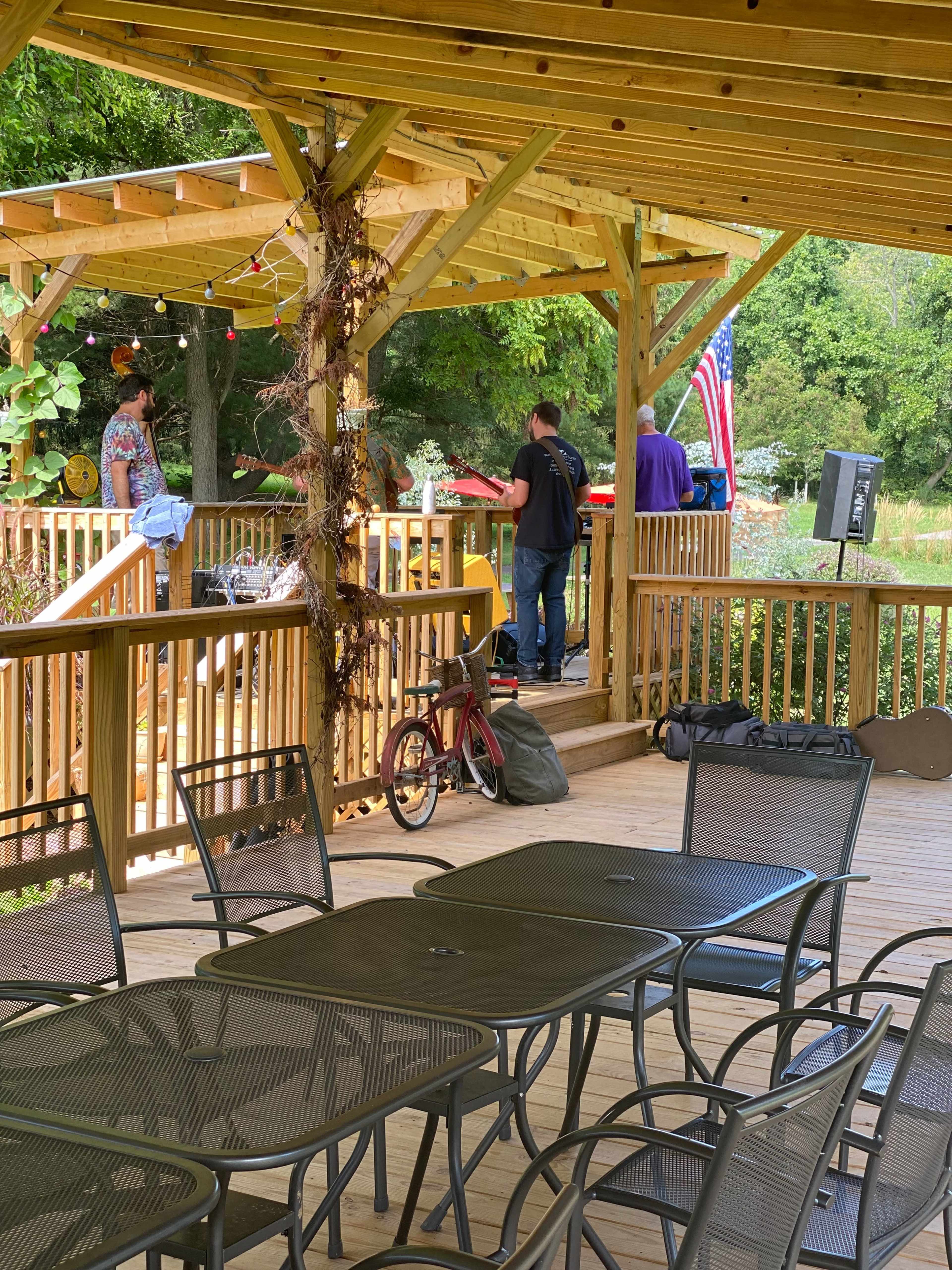 A wooden gazebo with people gathered around a table while a bicycle and bags are placed nearby on the deck.