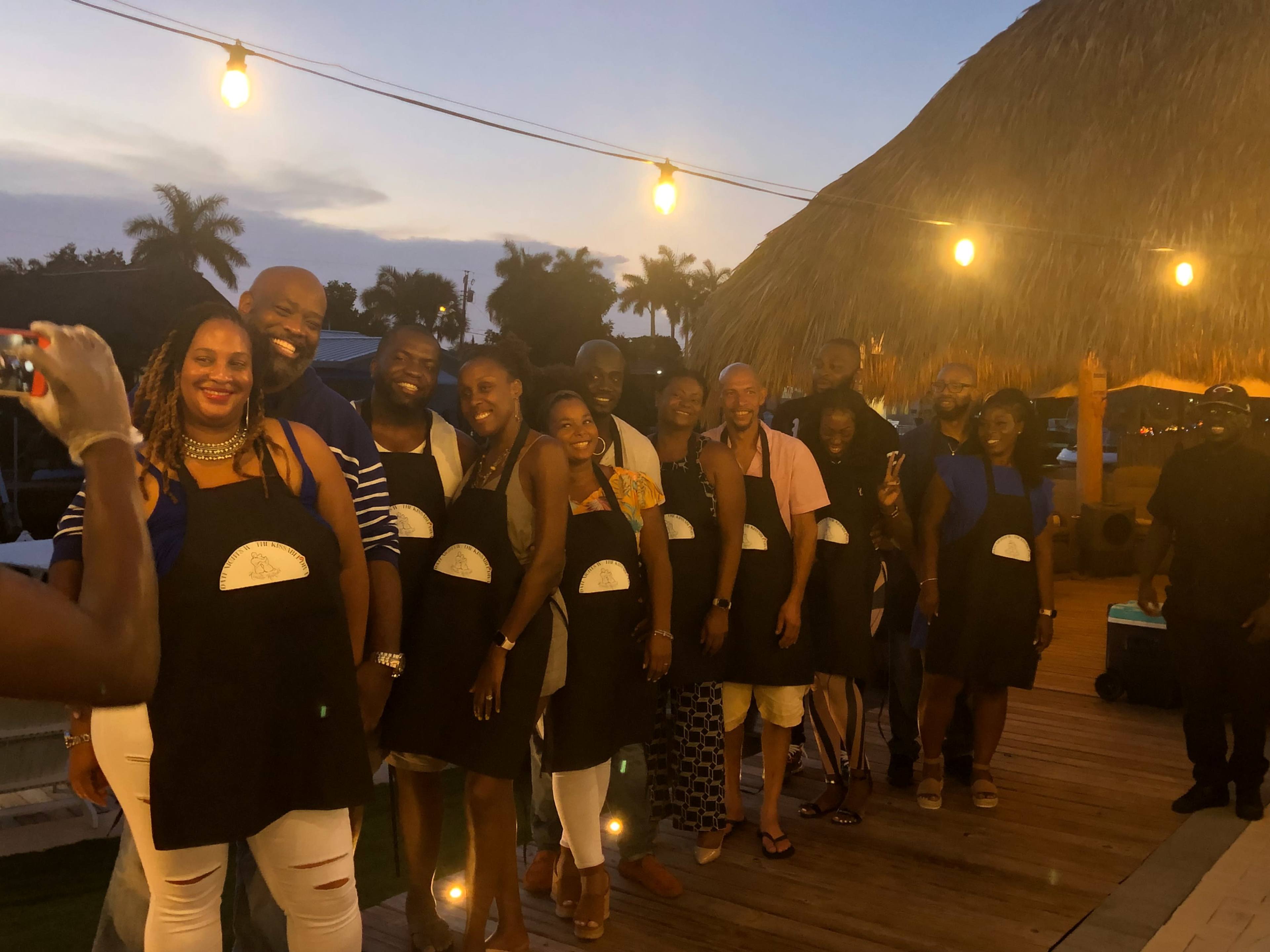 A group of people wearing matching aprons poses for a photo on an outdoor deck during sunset.