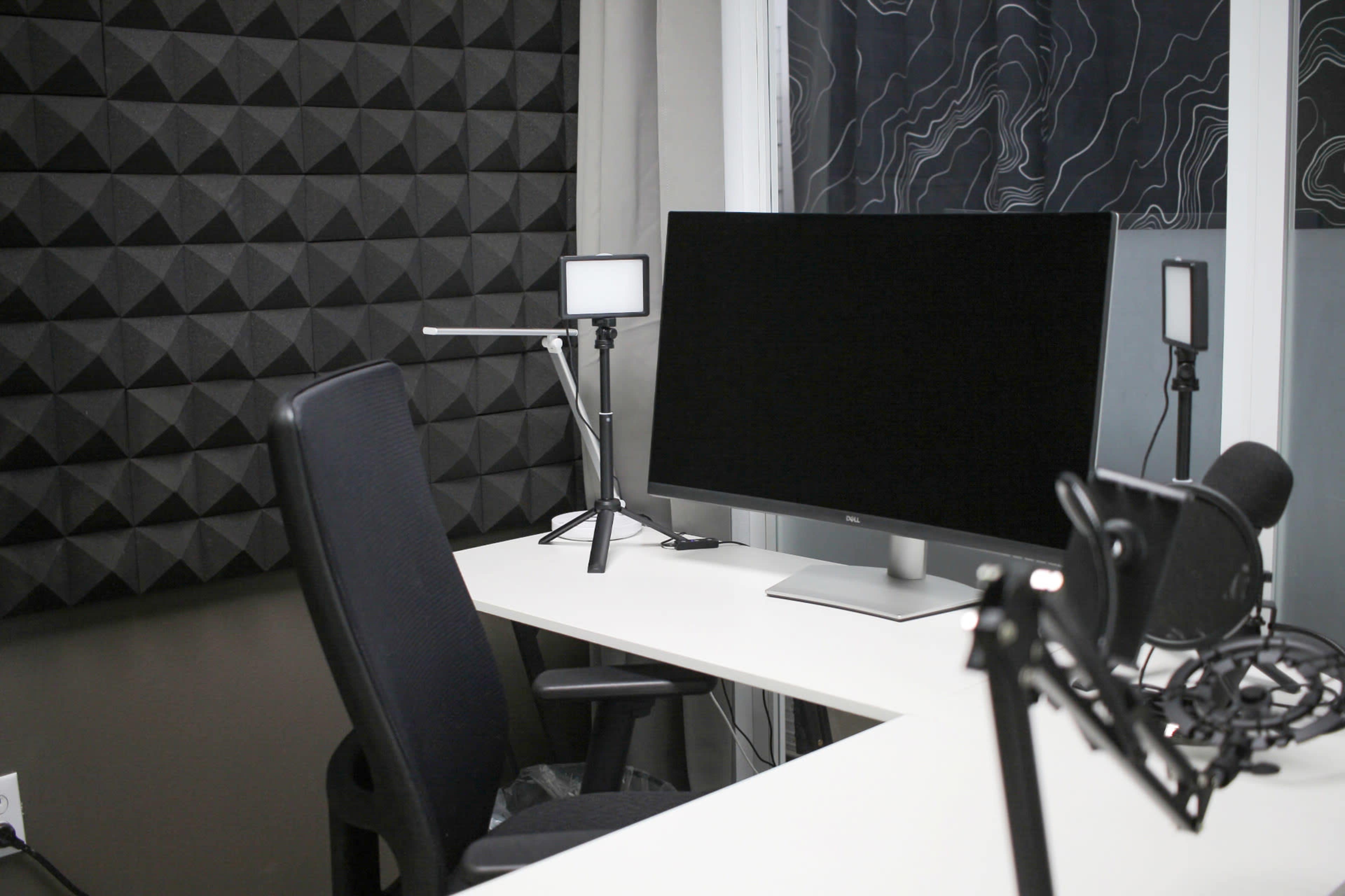 A modern workspace featuring a large monitor, a microphone setup, and soundproof paneling on the walls.