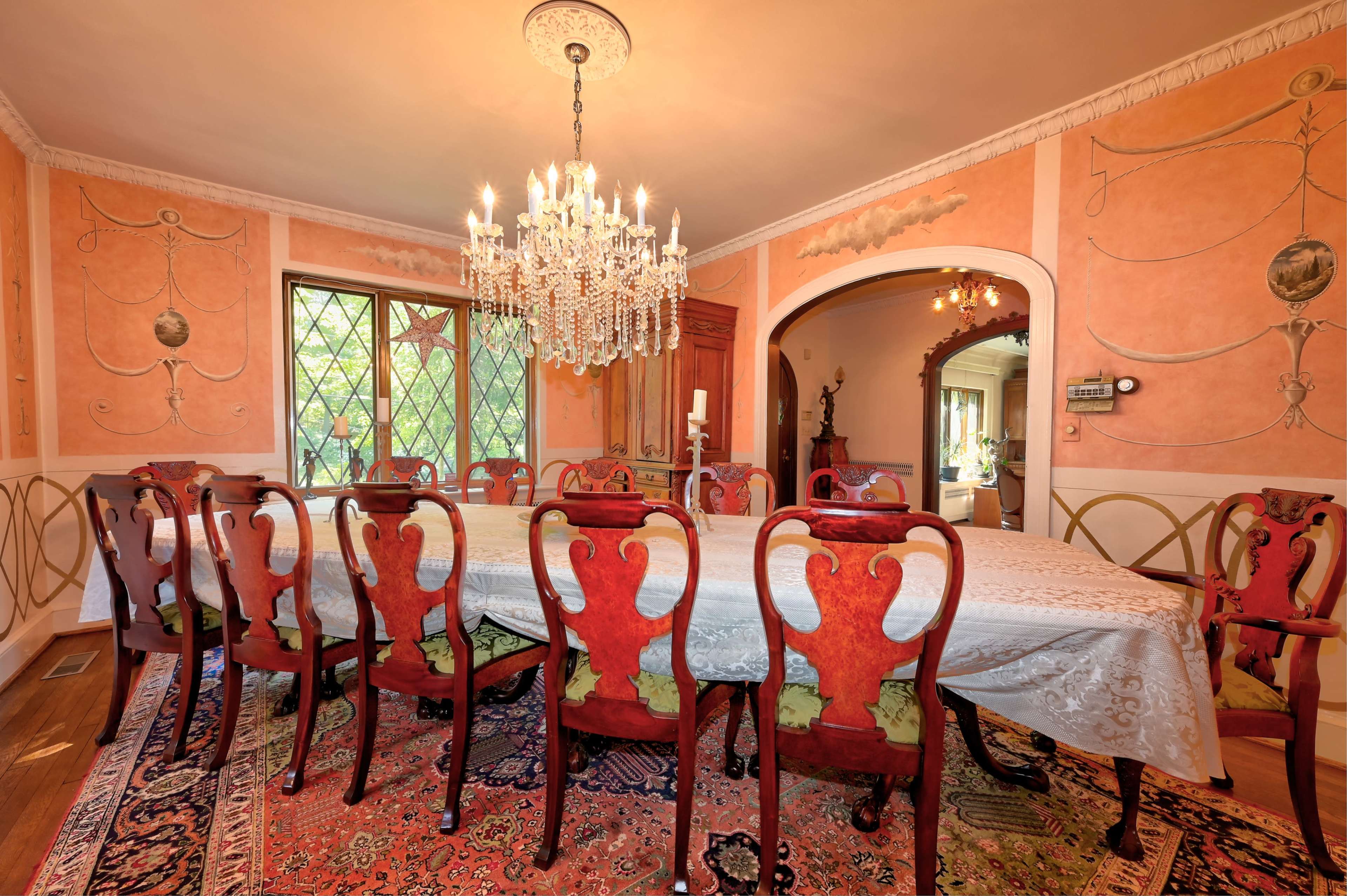 A spacious dining room with a large table surrounded by ornate red chairs and a chandelier overhead.