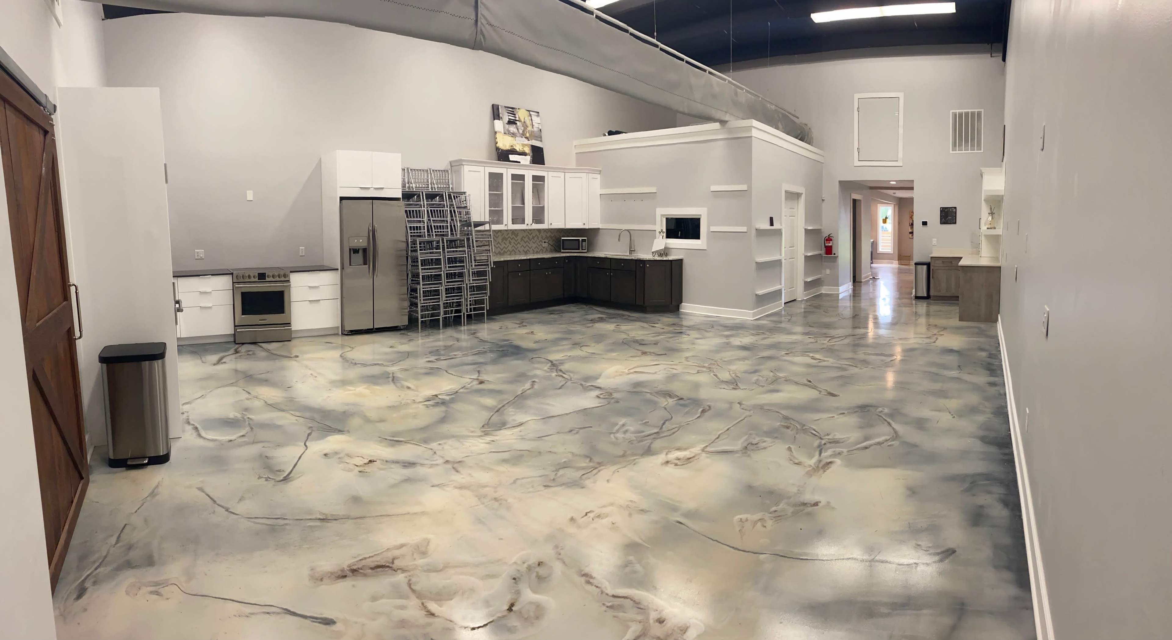 A spacious kitchen area featuring a modern design, with stainless steel appliances, white cabinets, and a polished concrete floor.