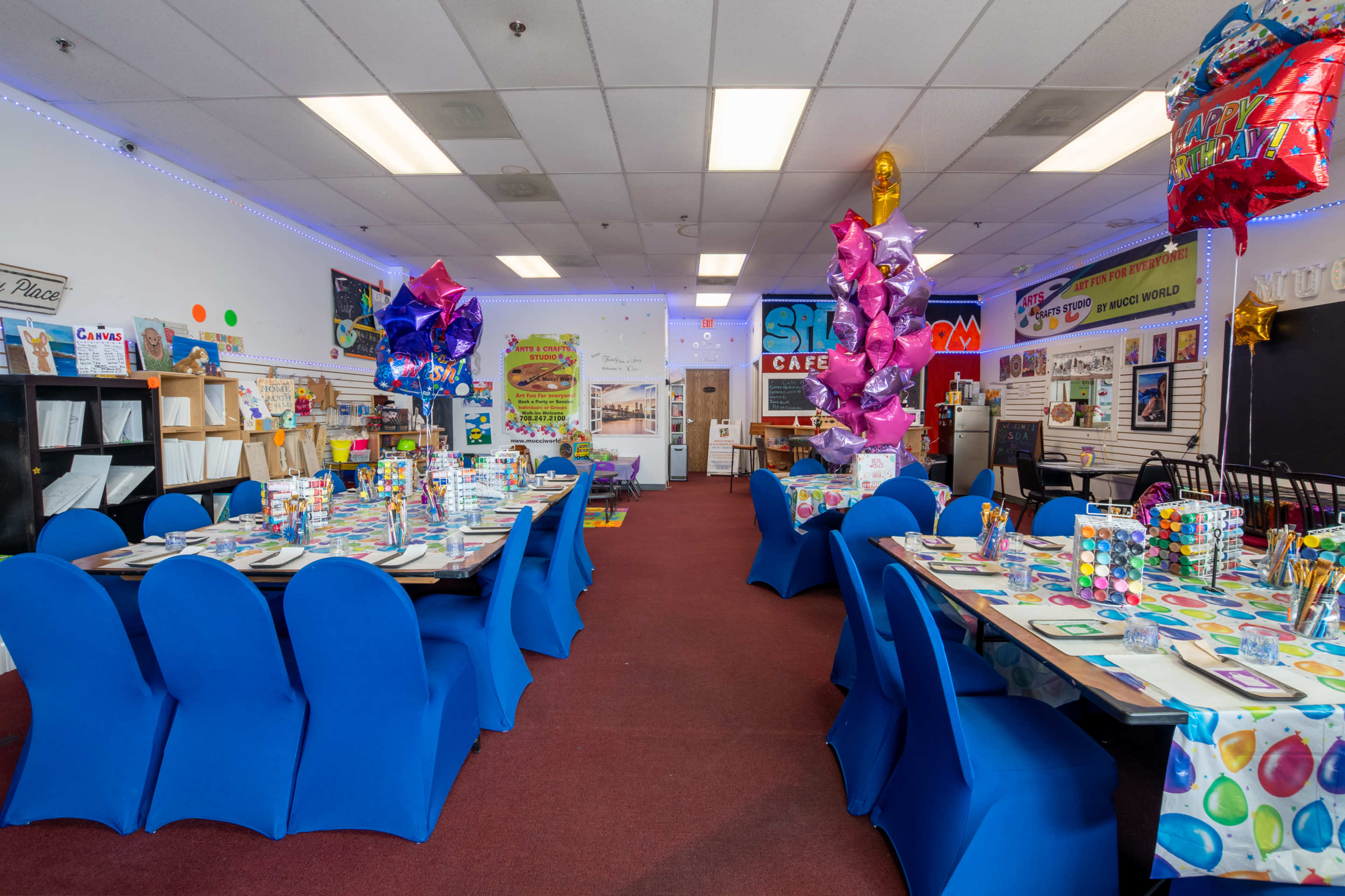 A brightly decorated cafe space features tables set with colorful items and balloons for a festive event.