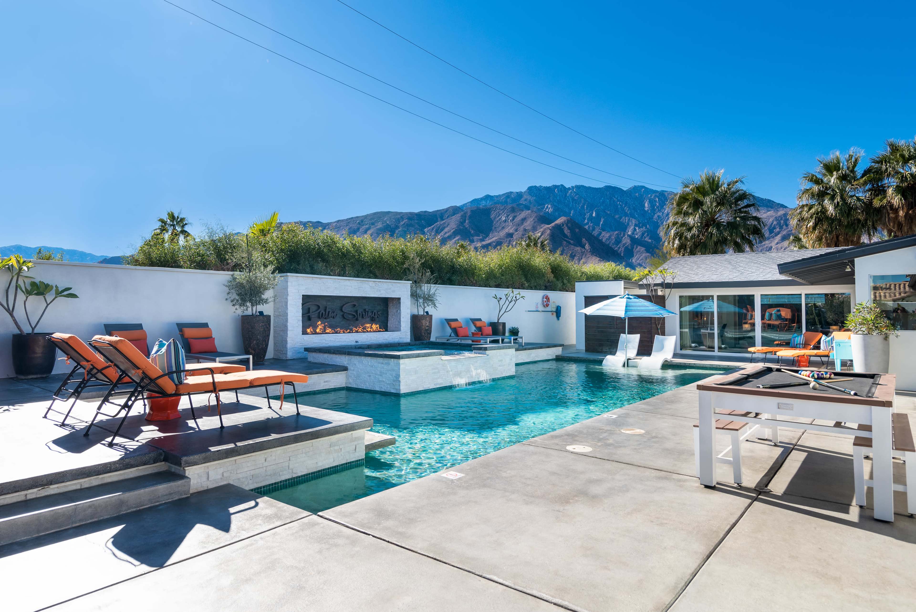 A modern backyard with a rectangular pool, lounge chairs, and a mountain backdrop.
