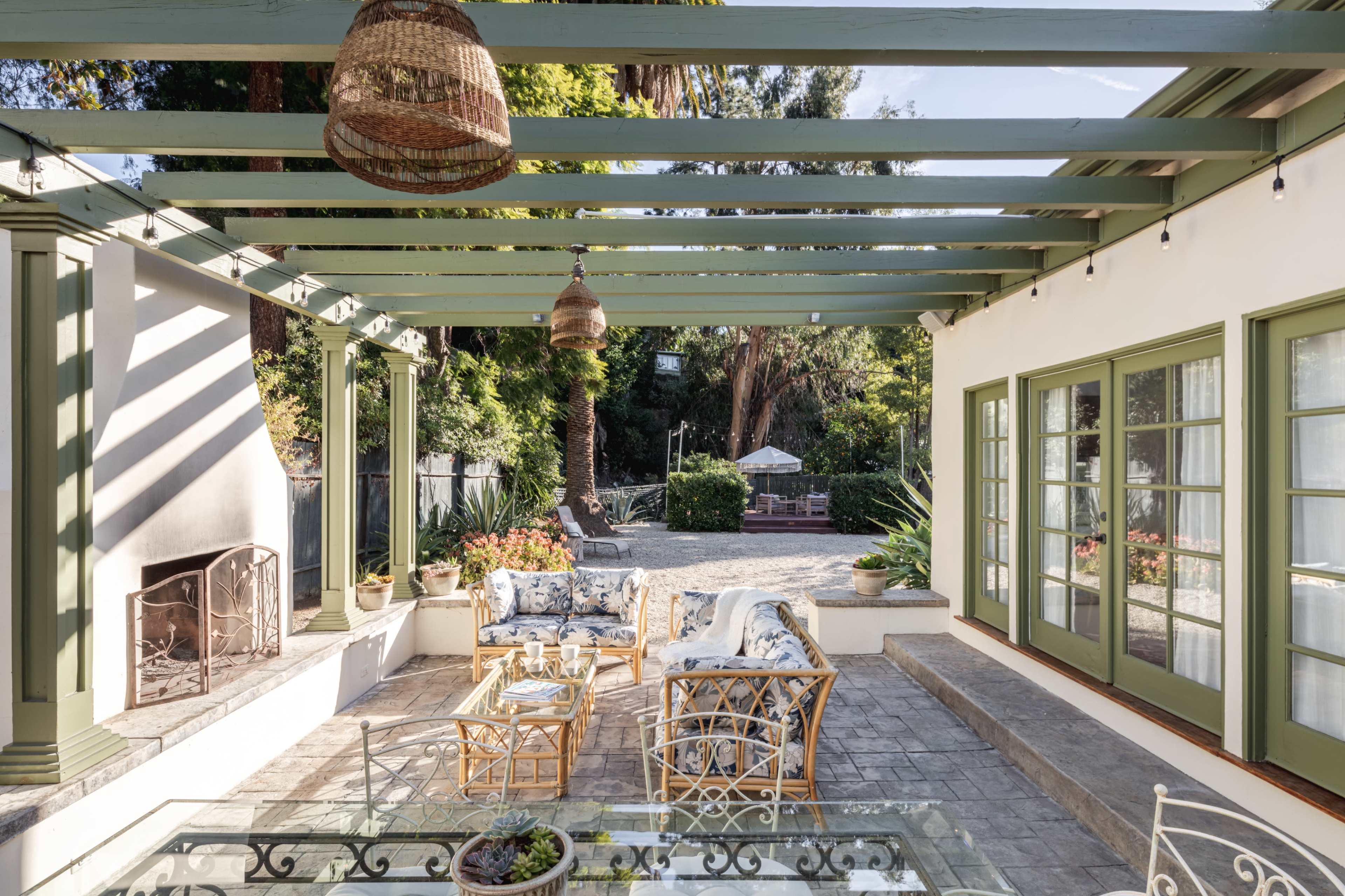 A spacious outdoor patio features a pergola, comfortable seating, and a stone floor, surrounded by greenery.