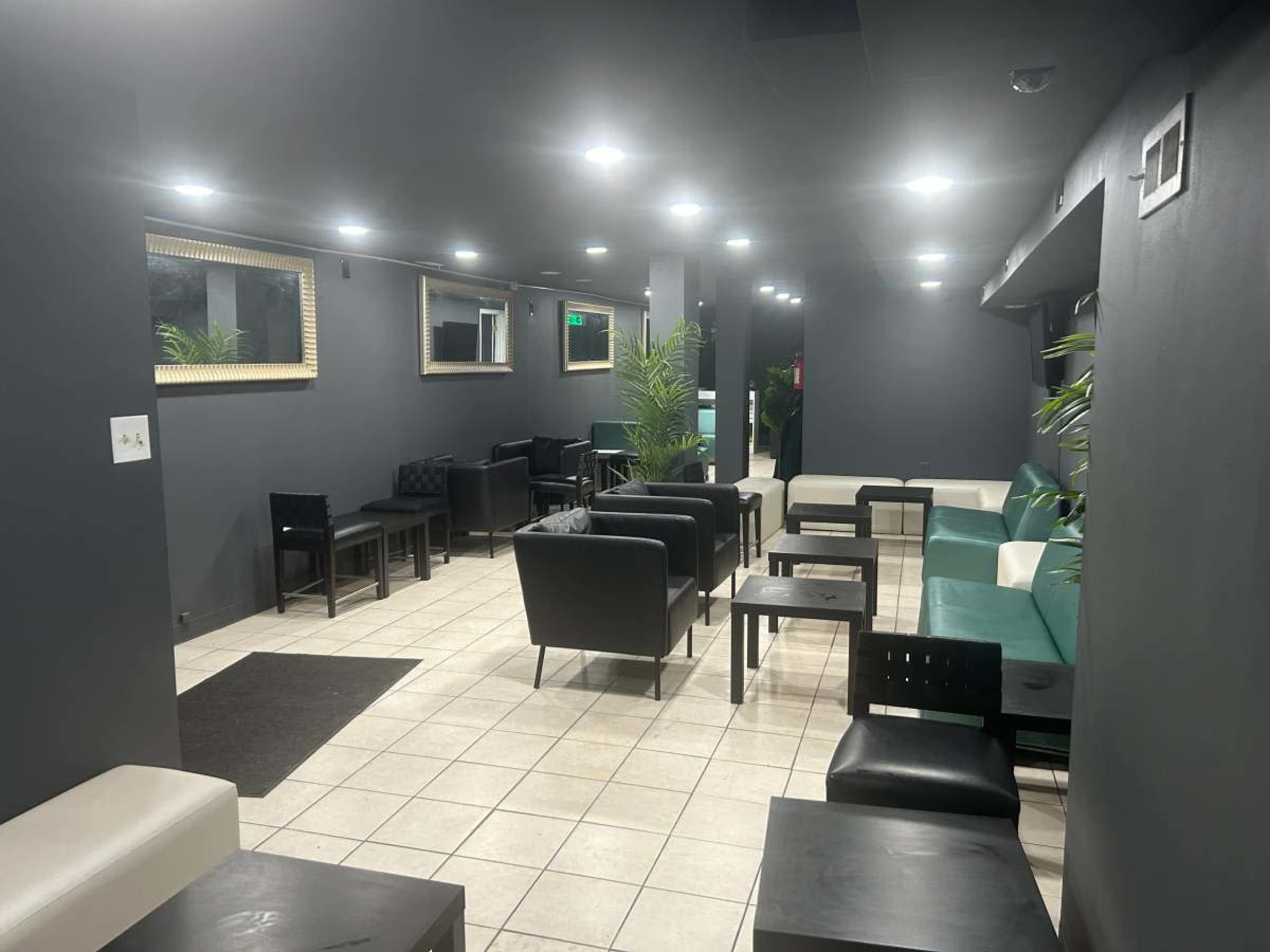 A modern lounge area with black and green seating, tiled flooring, and wall-mounted mirrors.