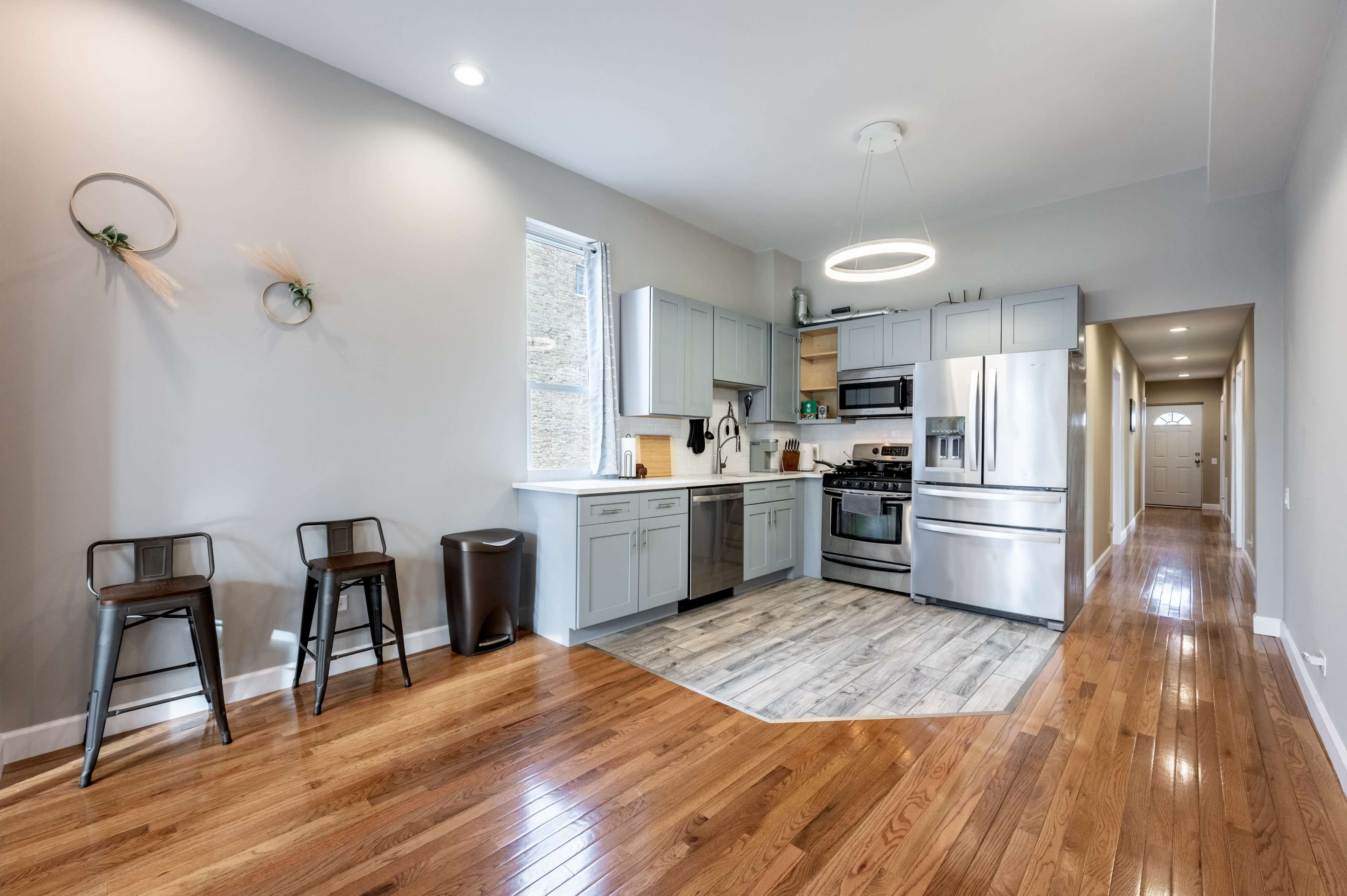 A modern kitchen with stainless steel appliances, a center island, and hardwood flooring that extends into a hallway.