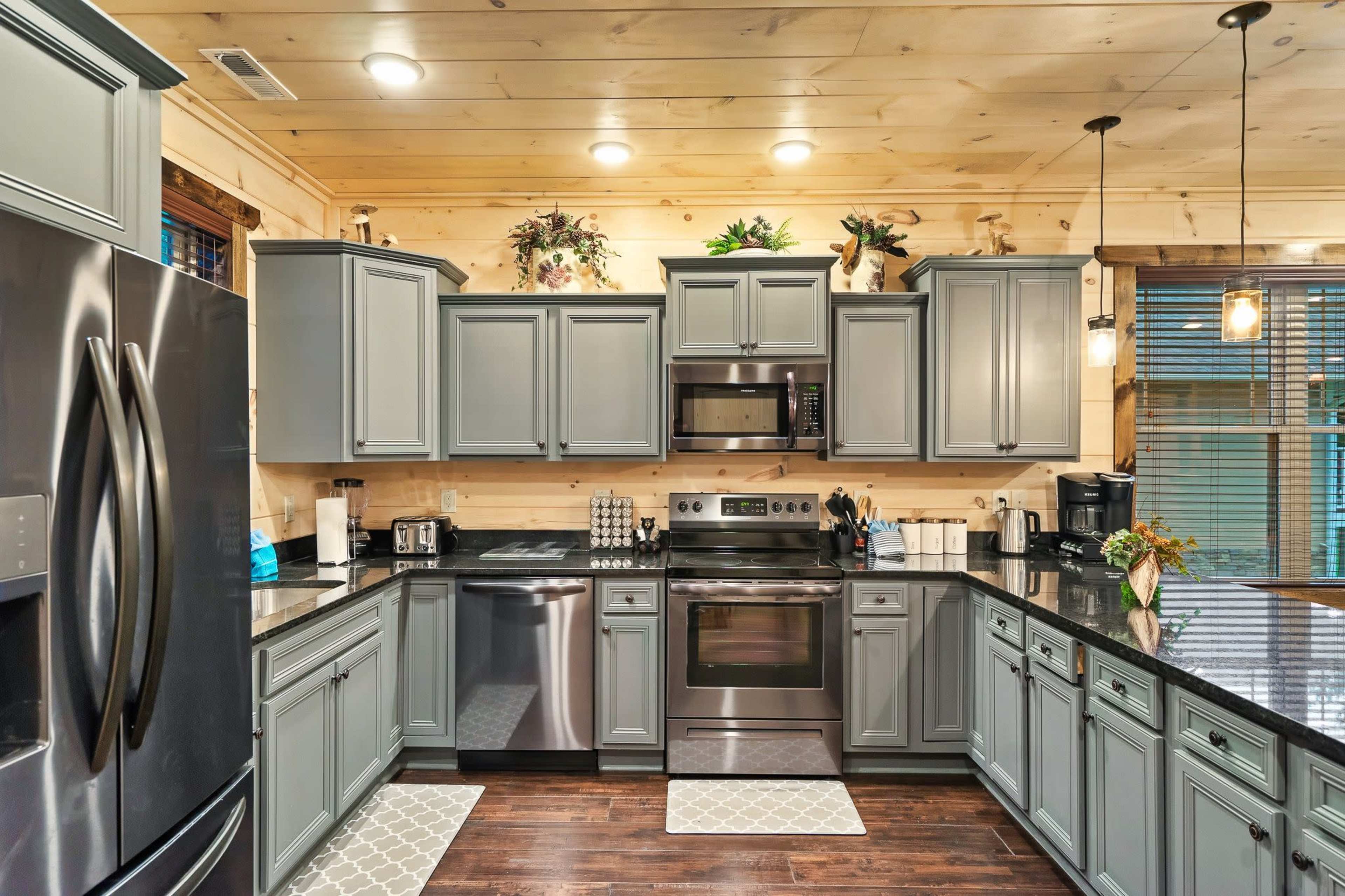 A modern kitchen features gray cabinets, stainless steel appliances, and a combination of dark countertops and light wooden walls.
