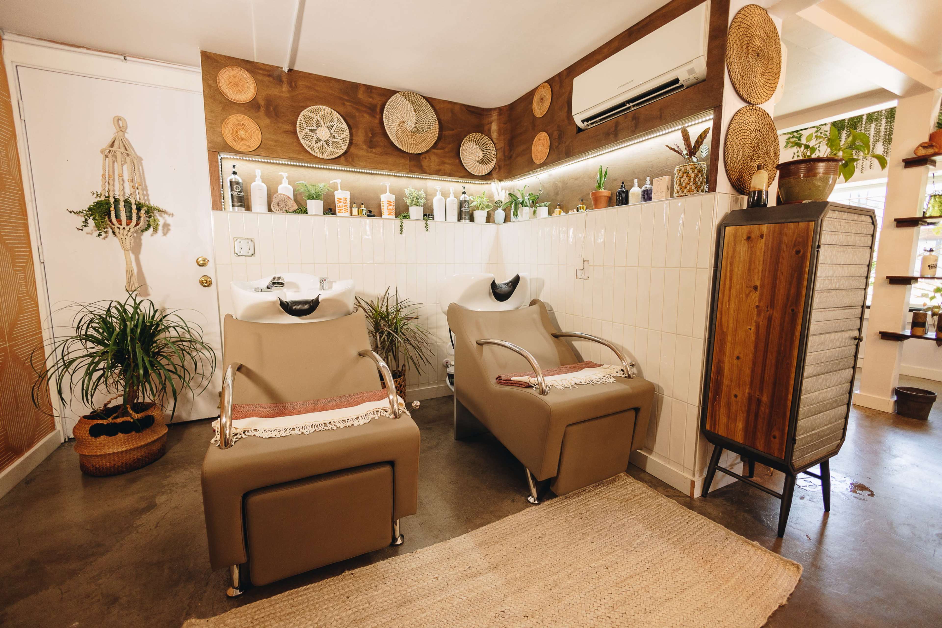 A modern hair salon setup with two shampoo chairs, potted plants, and decorative wall accents.