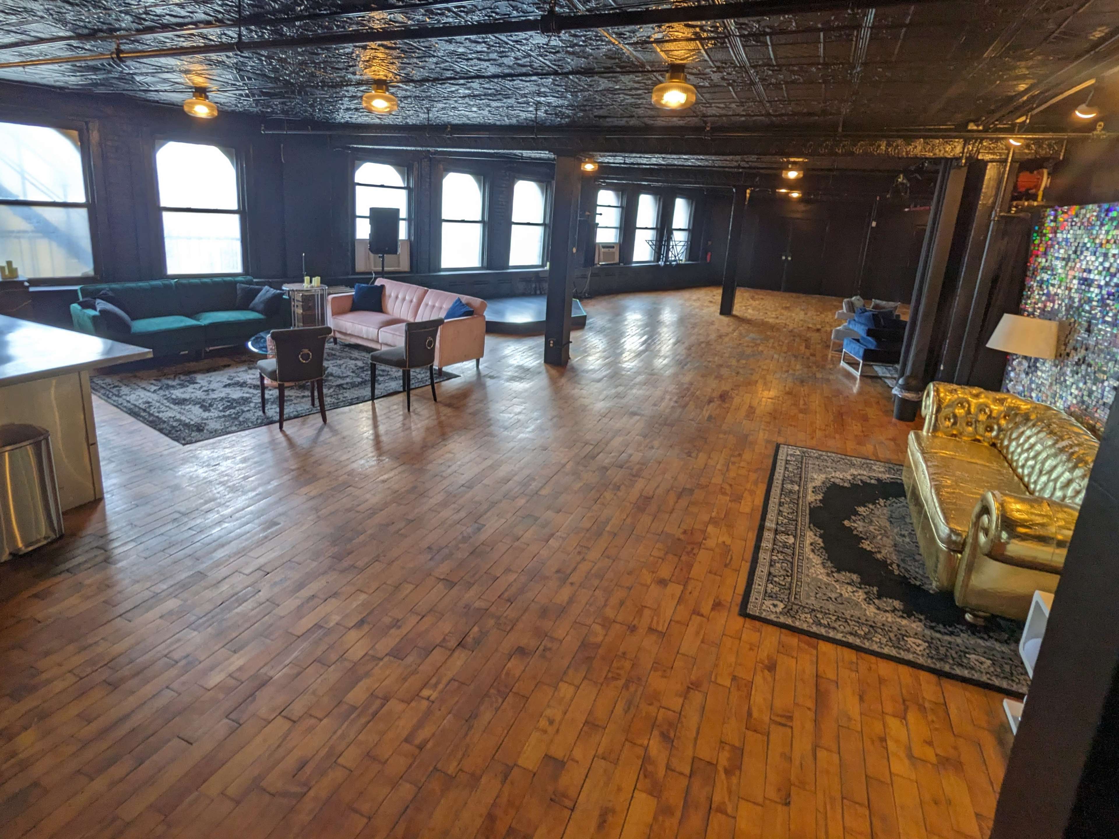 The spacious interior features a mix of seating arrangements, including a gold sofa and a pink couch, set against hardwood floors and large windows.