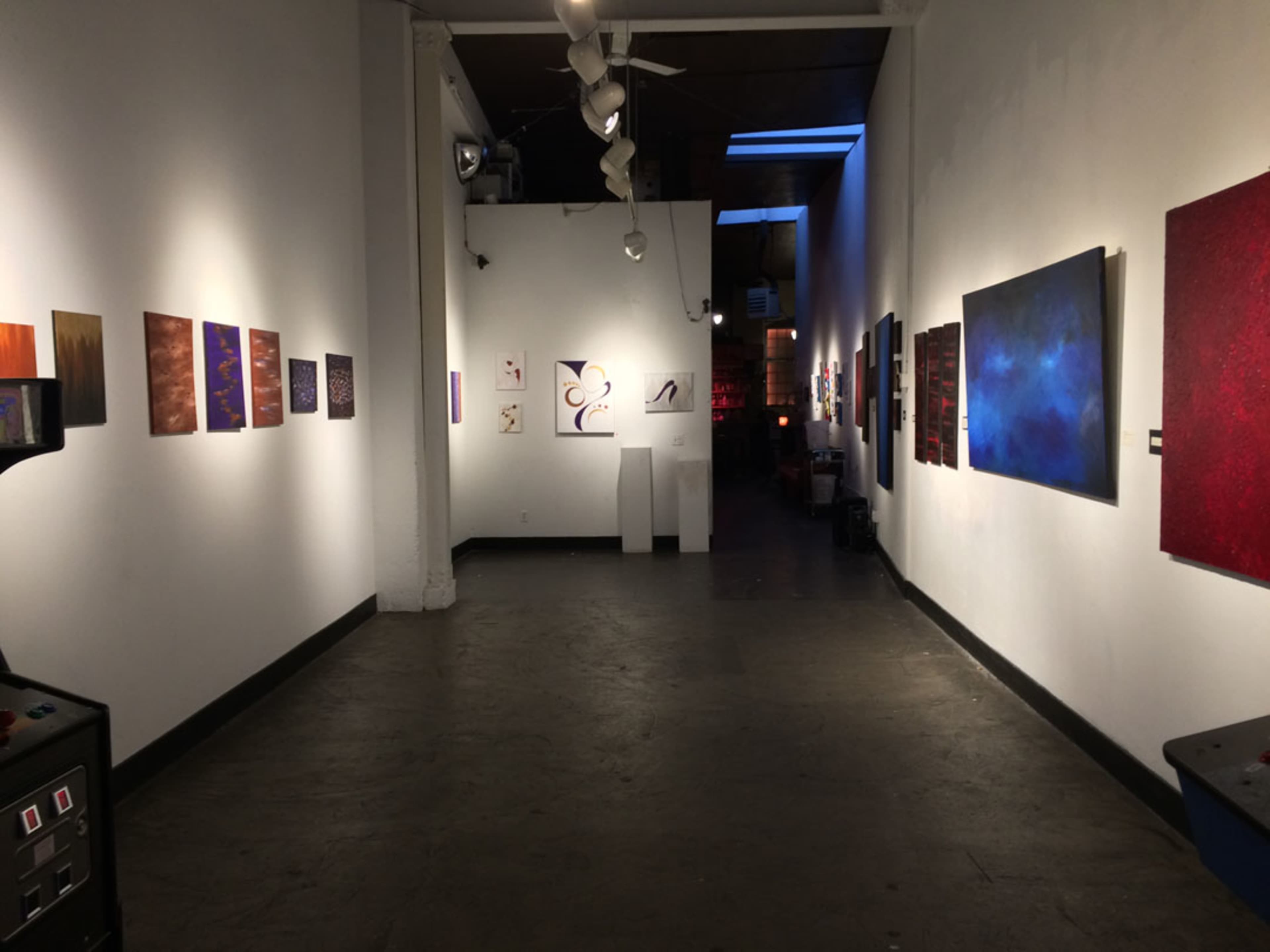 An art gallery with various framed artworks displayed on the walls and a dark floor.
