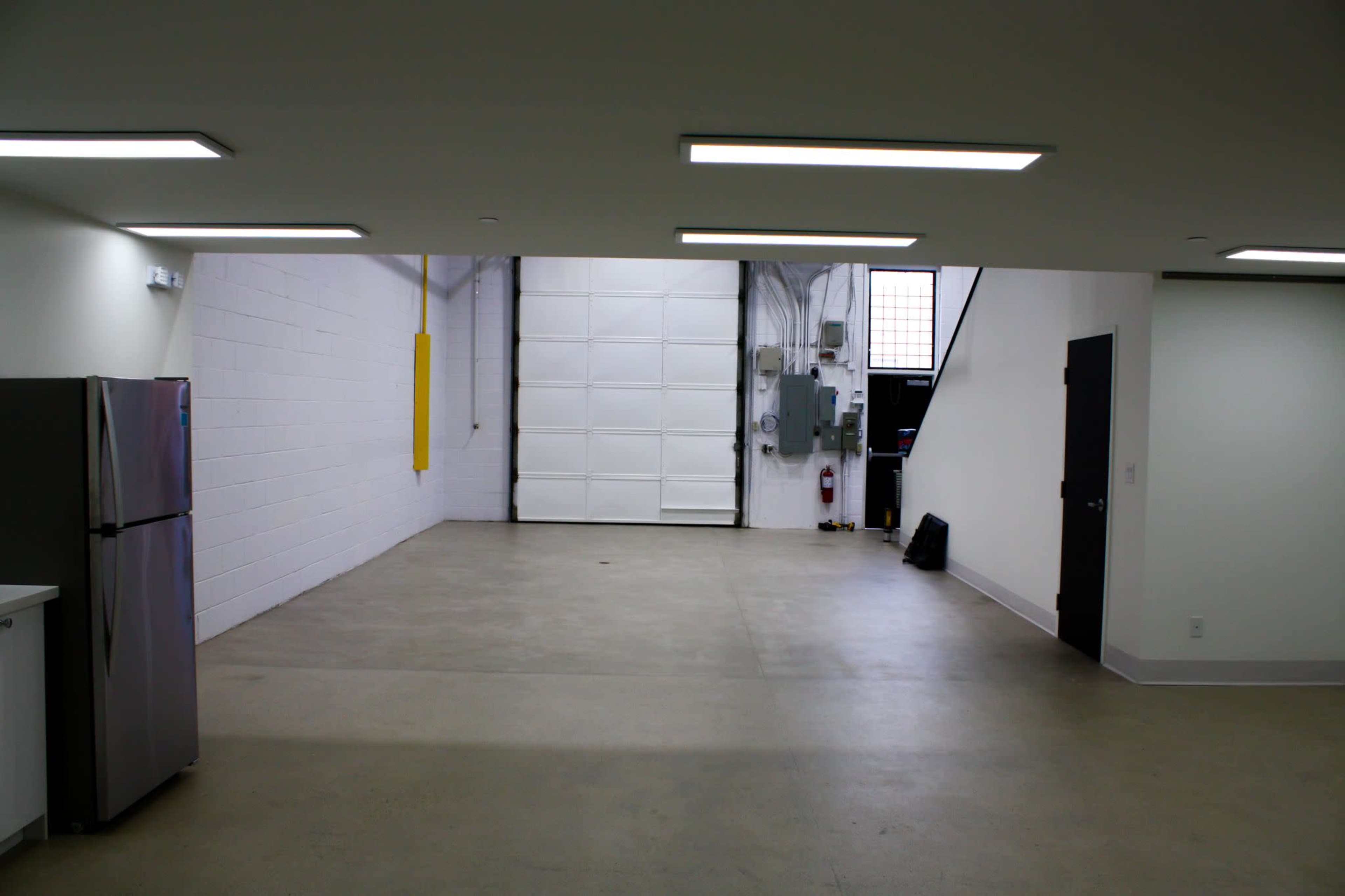 An empty, well-lit garage space with a large white garage door, concrete flooring, and minimal furnishings.