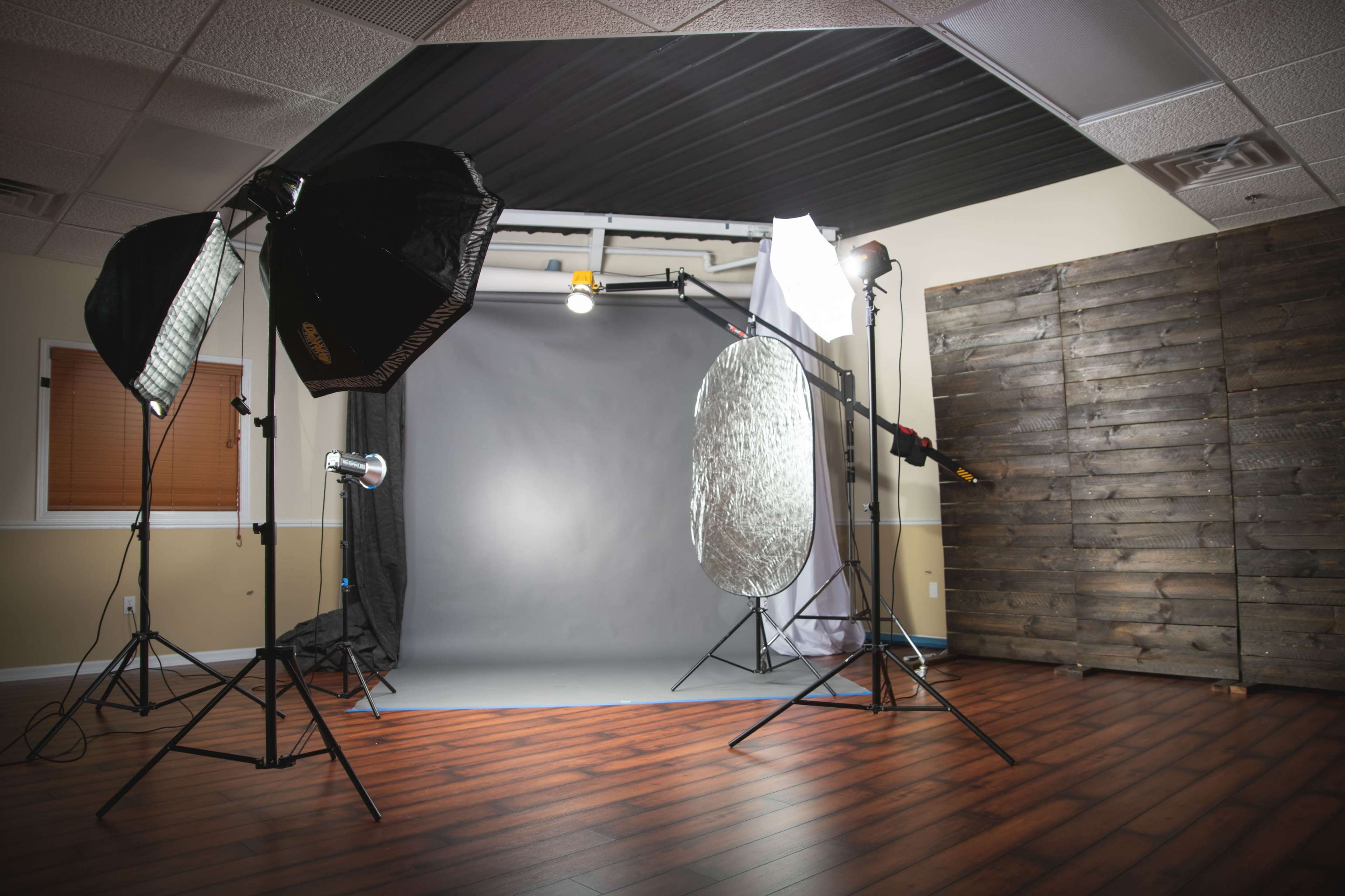 A photography studio with various lighting equipment set up around a gray backdrop and a wooden wall.