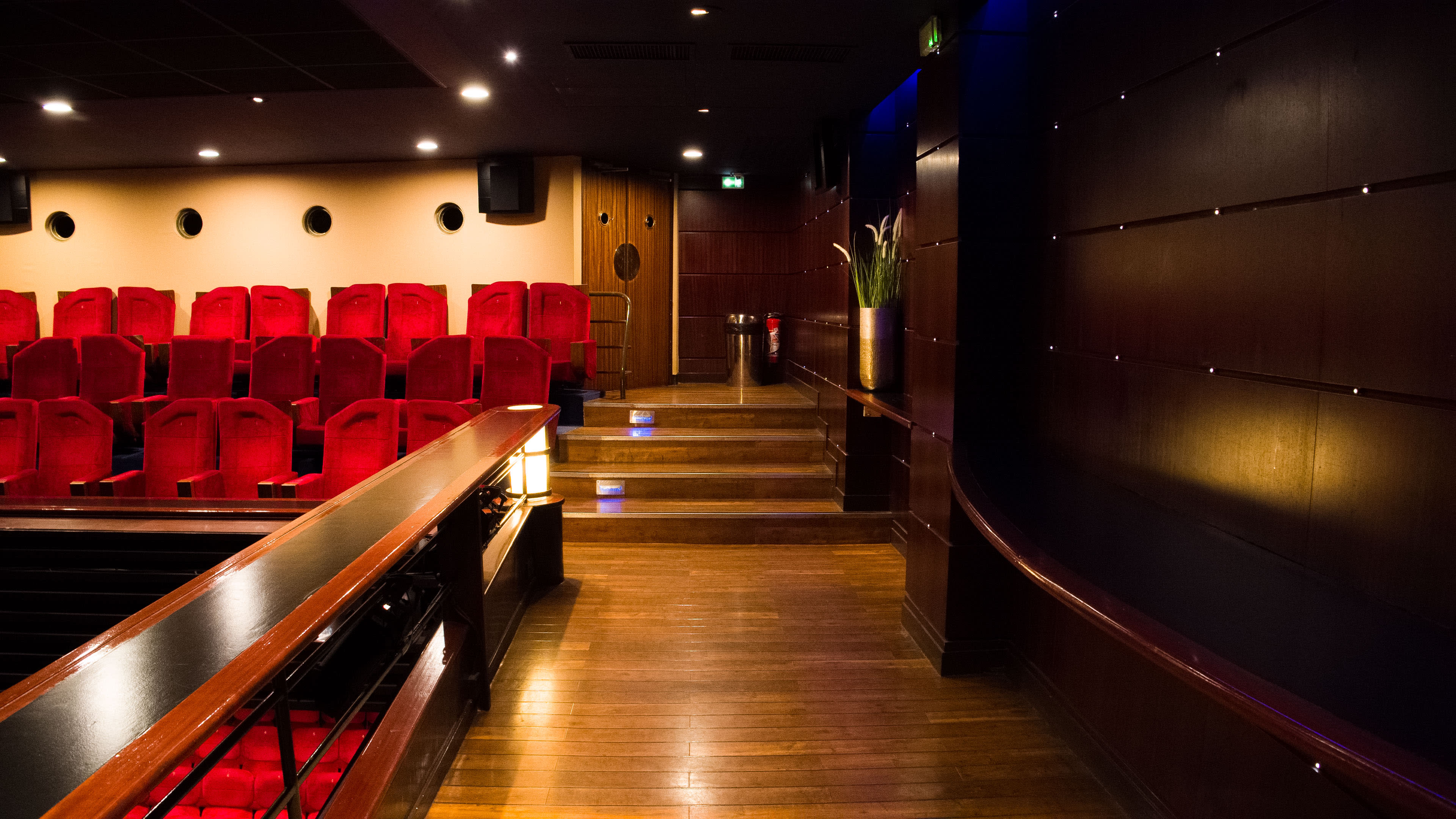 A dimly lit theater interior with red seating and wooden flooring.