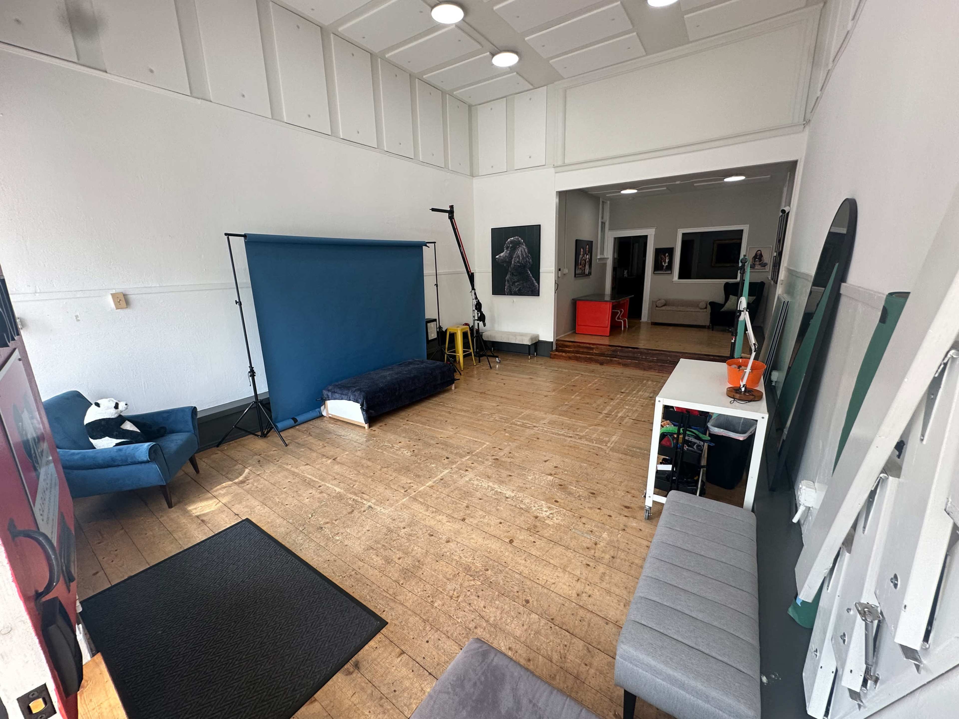 The image shows a spacious photography studio with a blue backdrop, wooden flooring, and various furniture including chairs and a table.