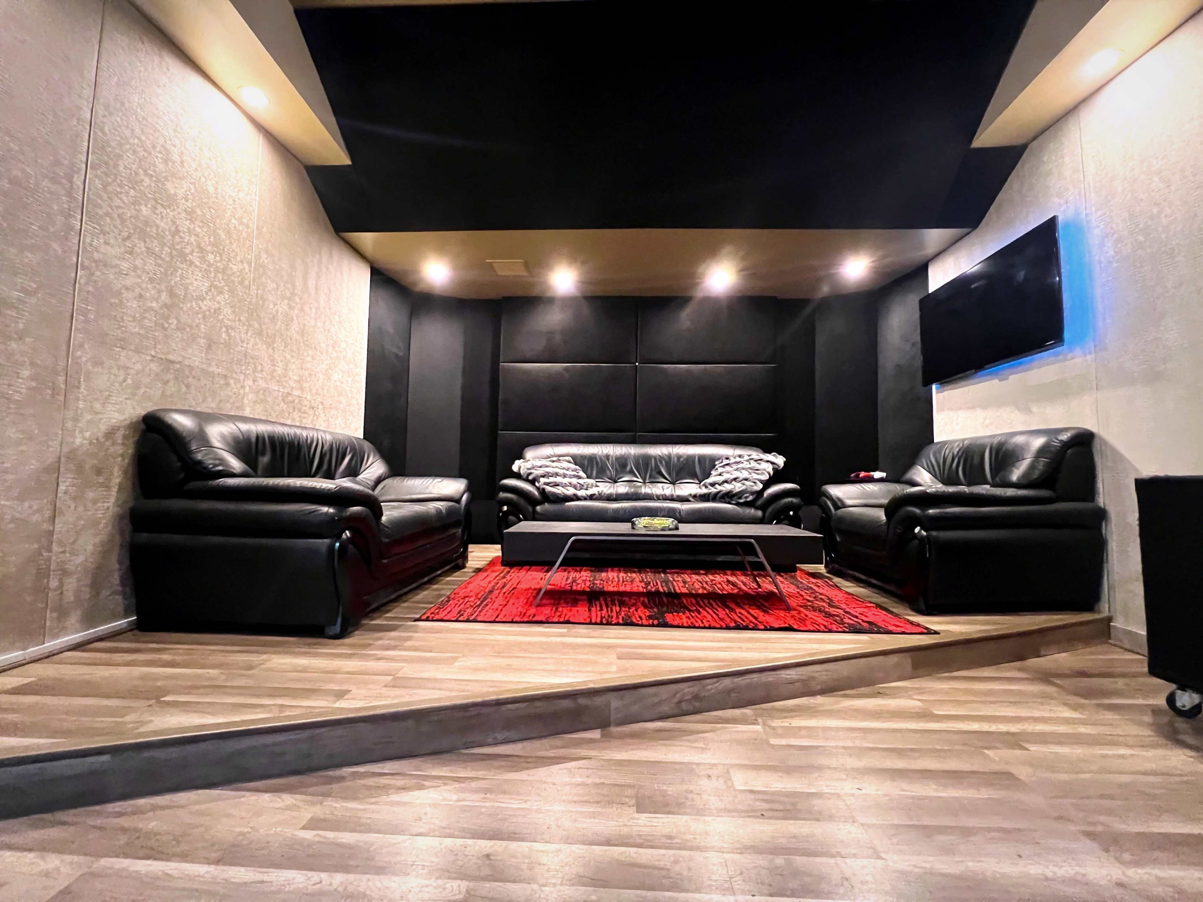 A modern lounge area with black leather sofas, a red rug, a glass coffee table, and a wall-mounted television.