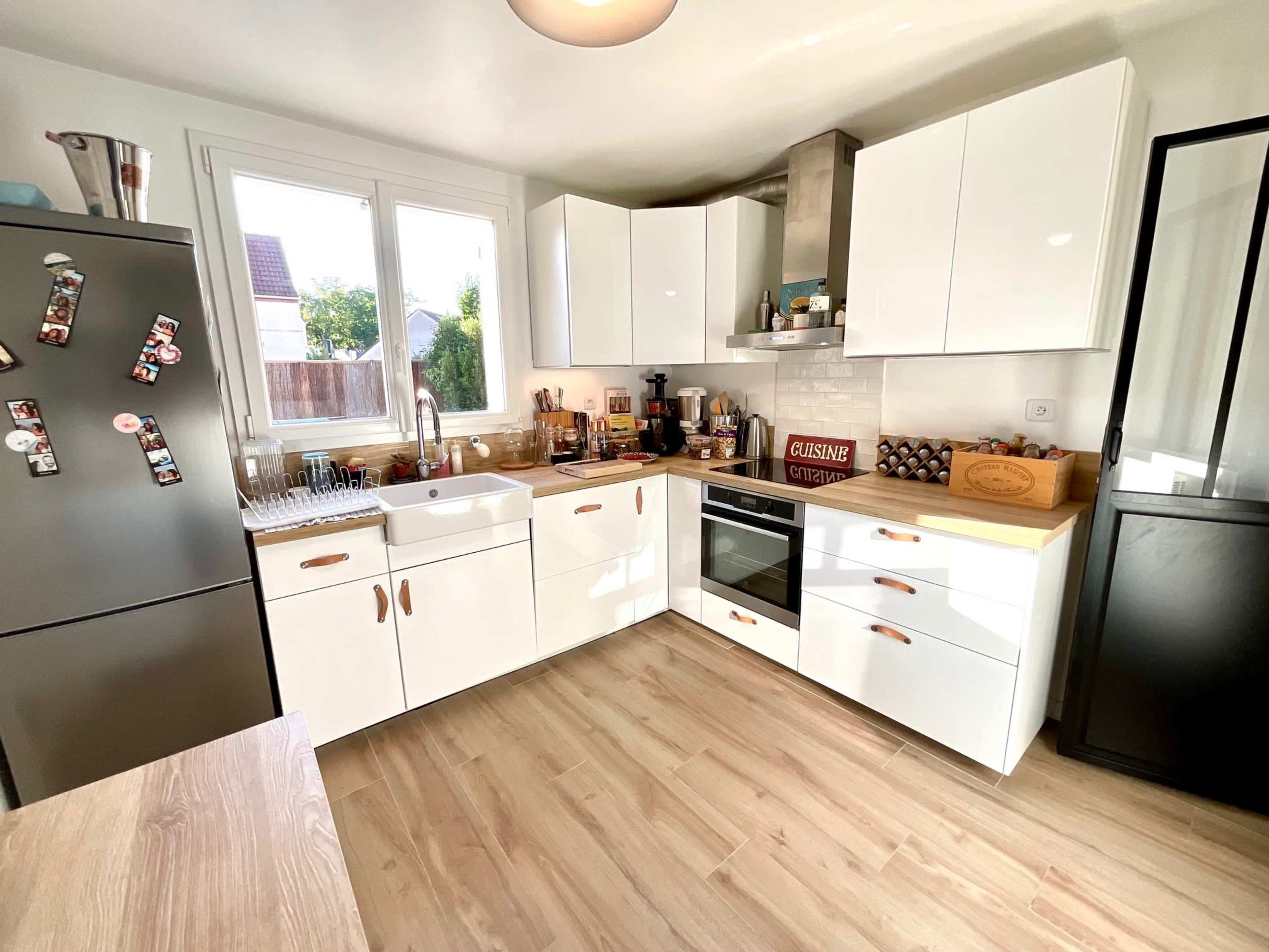 A modern kitchen features white cabinets, a stainless steel oven, a large sink, and wooden countertops with various kitchen tools and decorations.