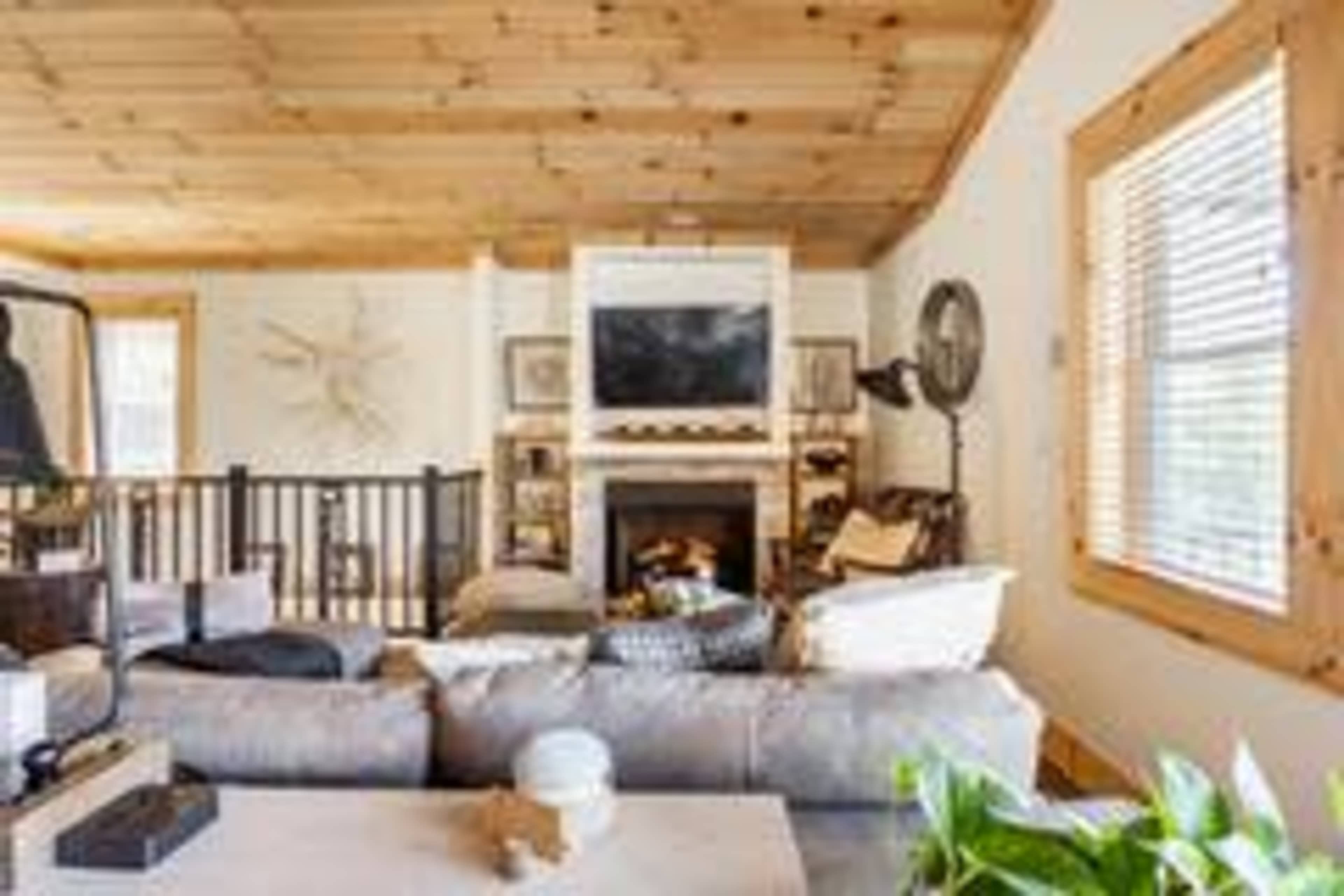 A cozy living room with a fireplace, a large sofa, and wooden ceiling beams.