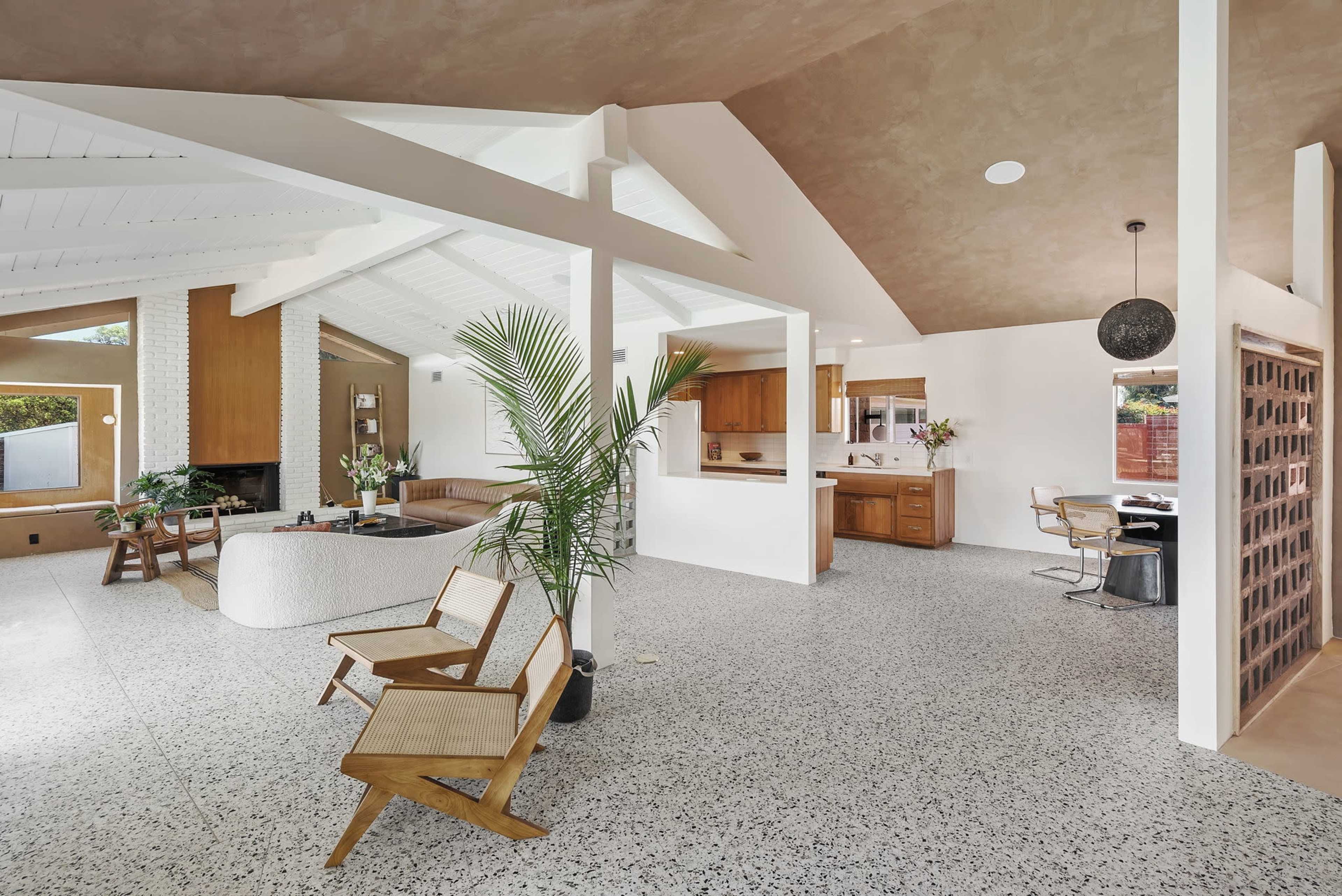 The image shows a spacious, modern interior featuring an open living area with a unique seating arrangement, a kitchen area, and large windows allowing natural light to enter.