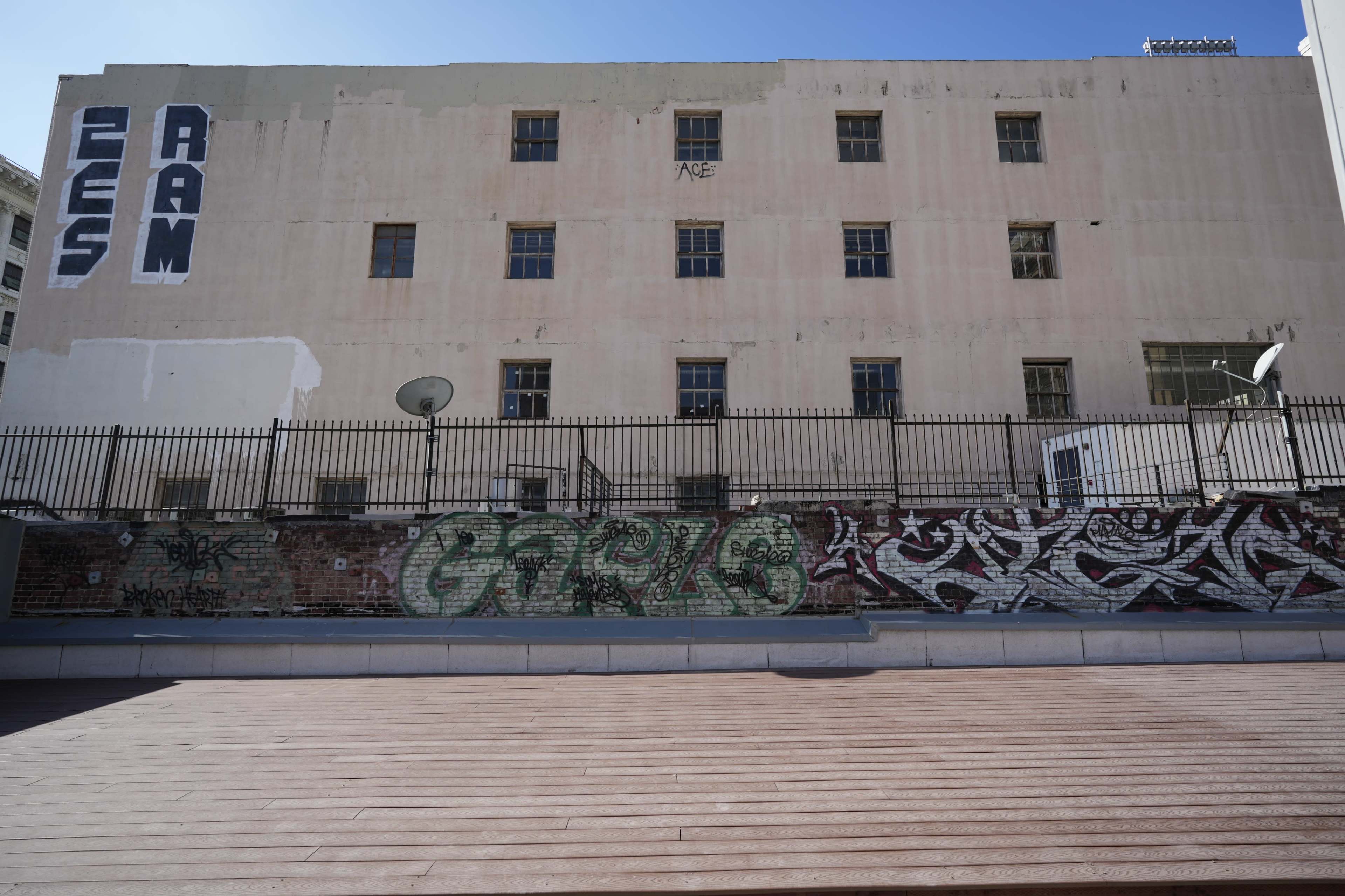 A plain building with faded paint features various graffiti designs on its lower wall.