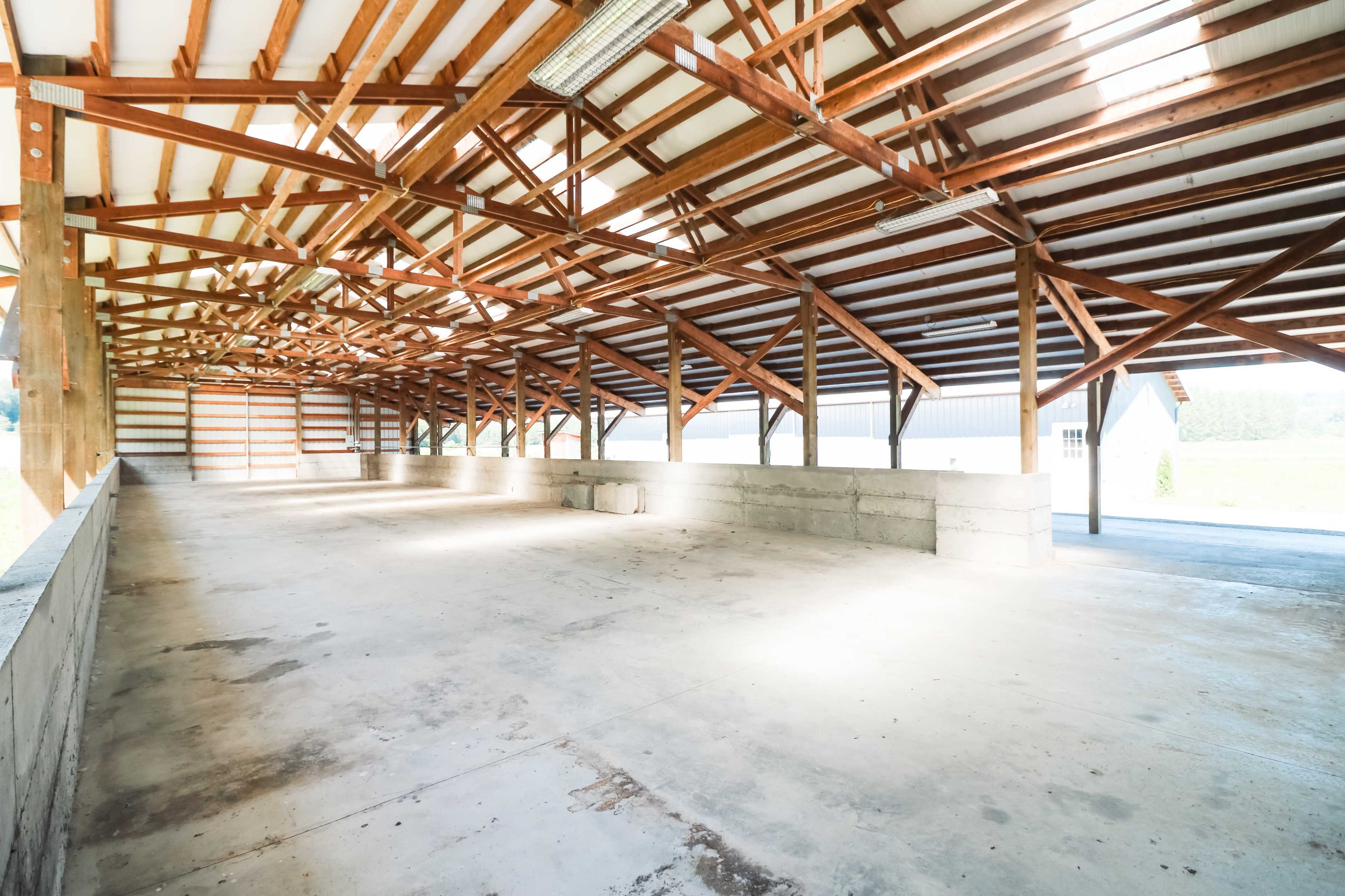 The image shows a spacious, empty barn with exposed wooden beams and a concrete floor.