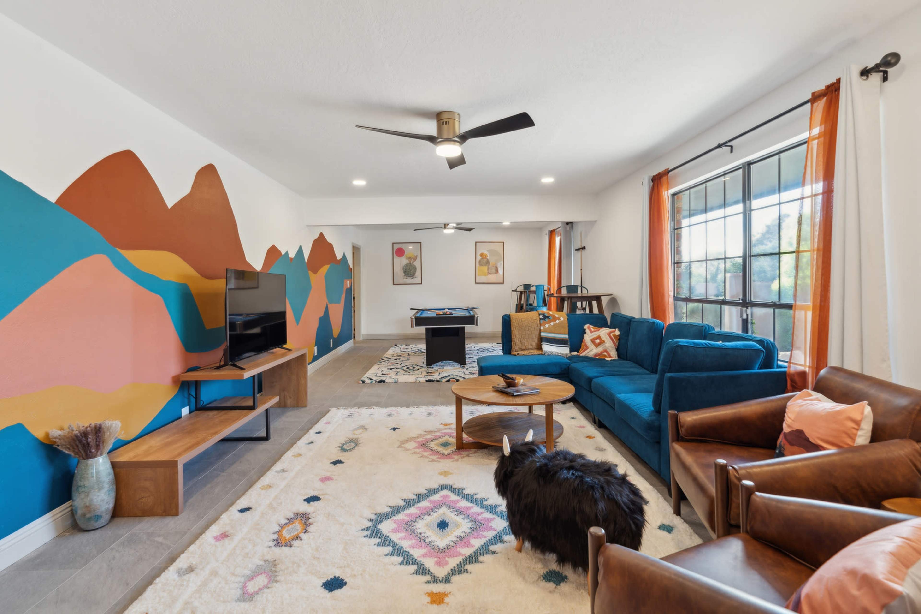 A spacious living room features colorful wall art, a large area rug, a blue couch, and a pool table in the background.