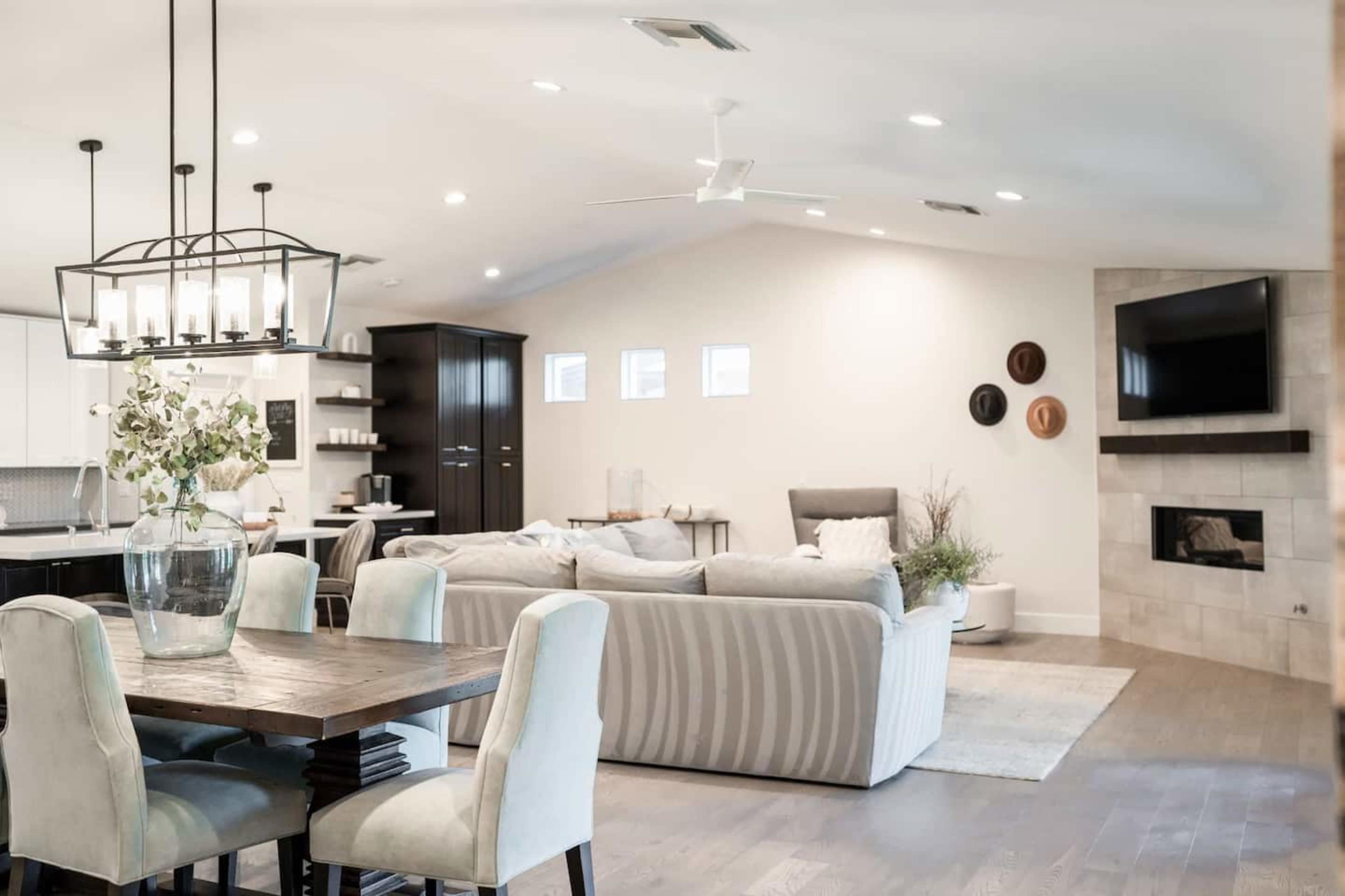 A spacious living area features a dining table, a sectional sofa, and a modern fireplace, with large windows allowing natural light to fill the room.