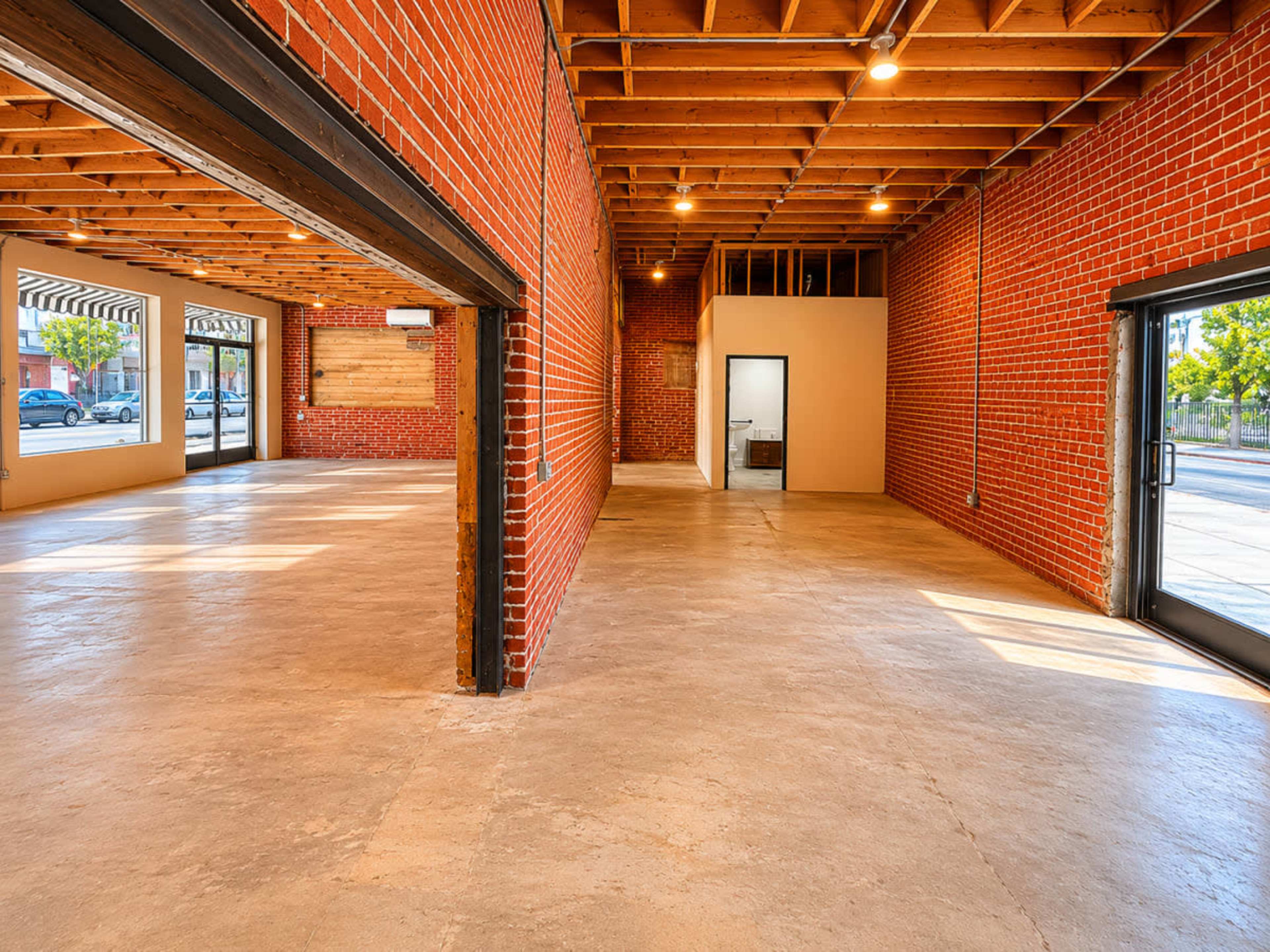 The image shows an empty commercial space with exposed brick walls and a concrete floor.