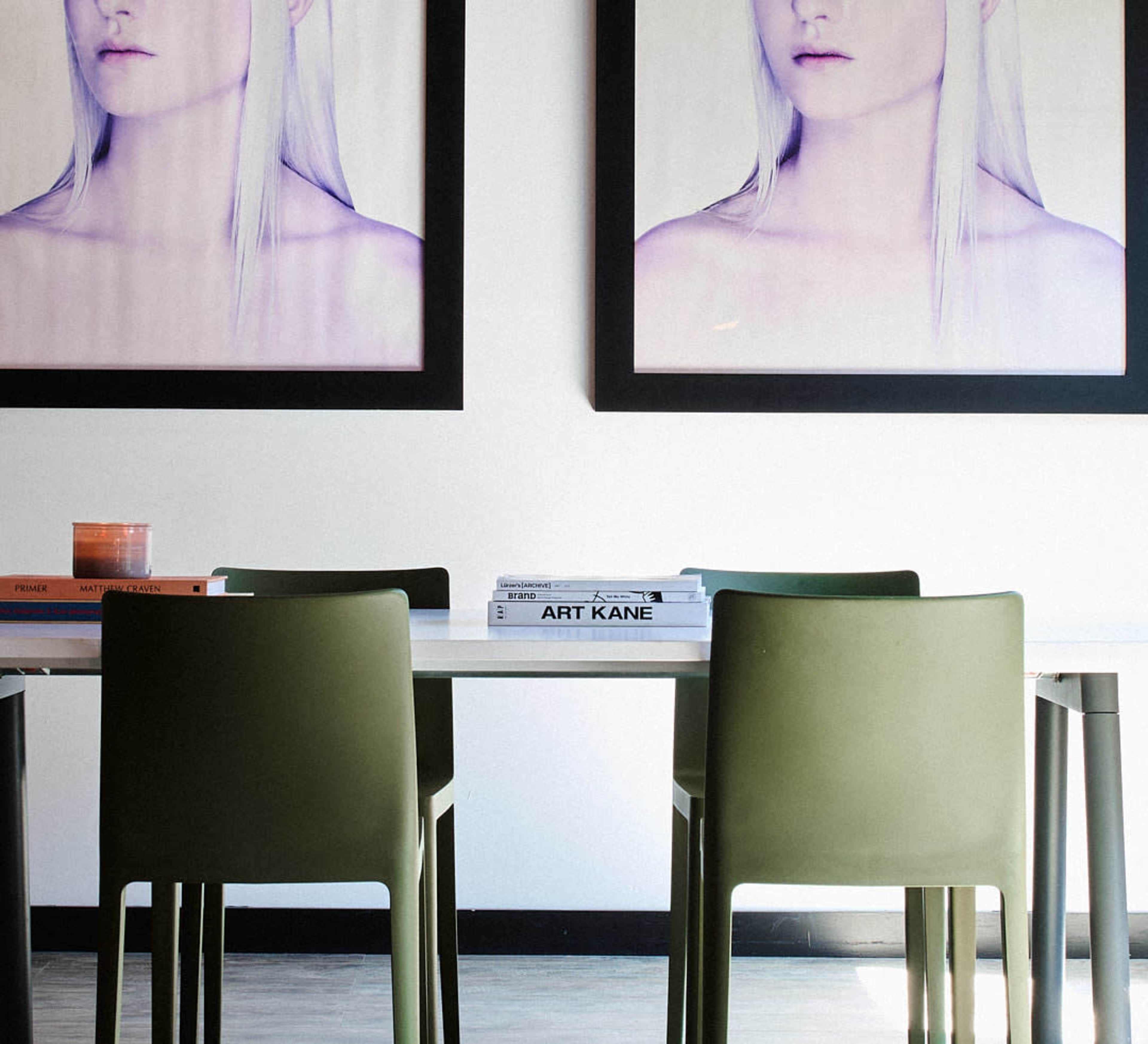 A dining table with four green chairs is positioned in front of two large framed portraits on the wall.