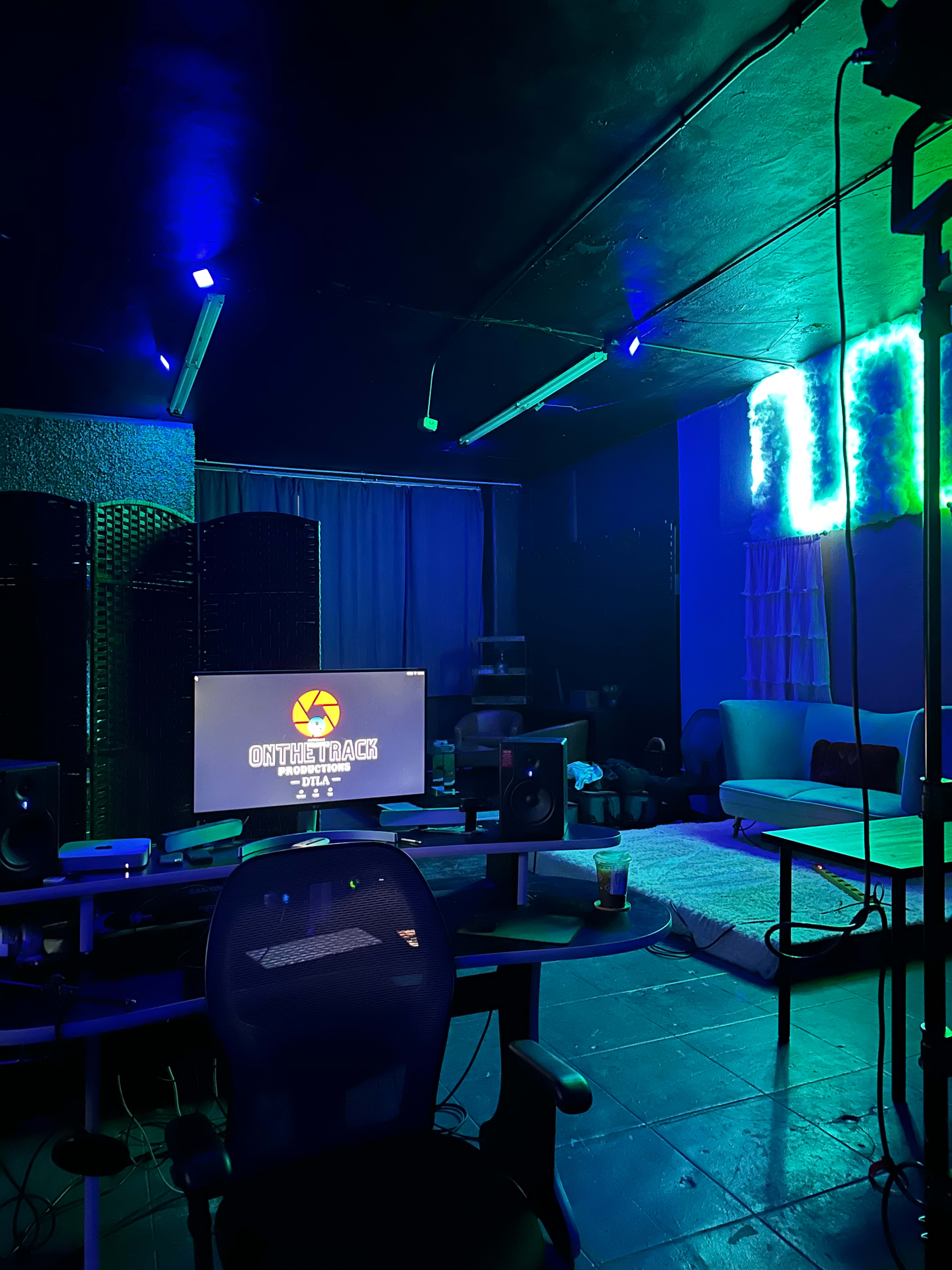 A dimly lit room with blue LED lighting, featuring a computer desk with a monitor displaying "ON THE TRACK" and a large white area rug on the floor.