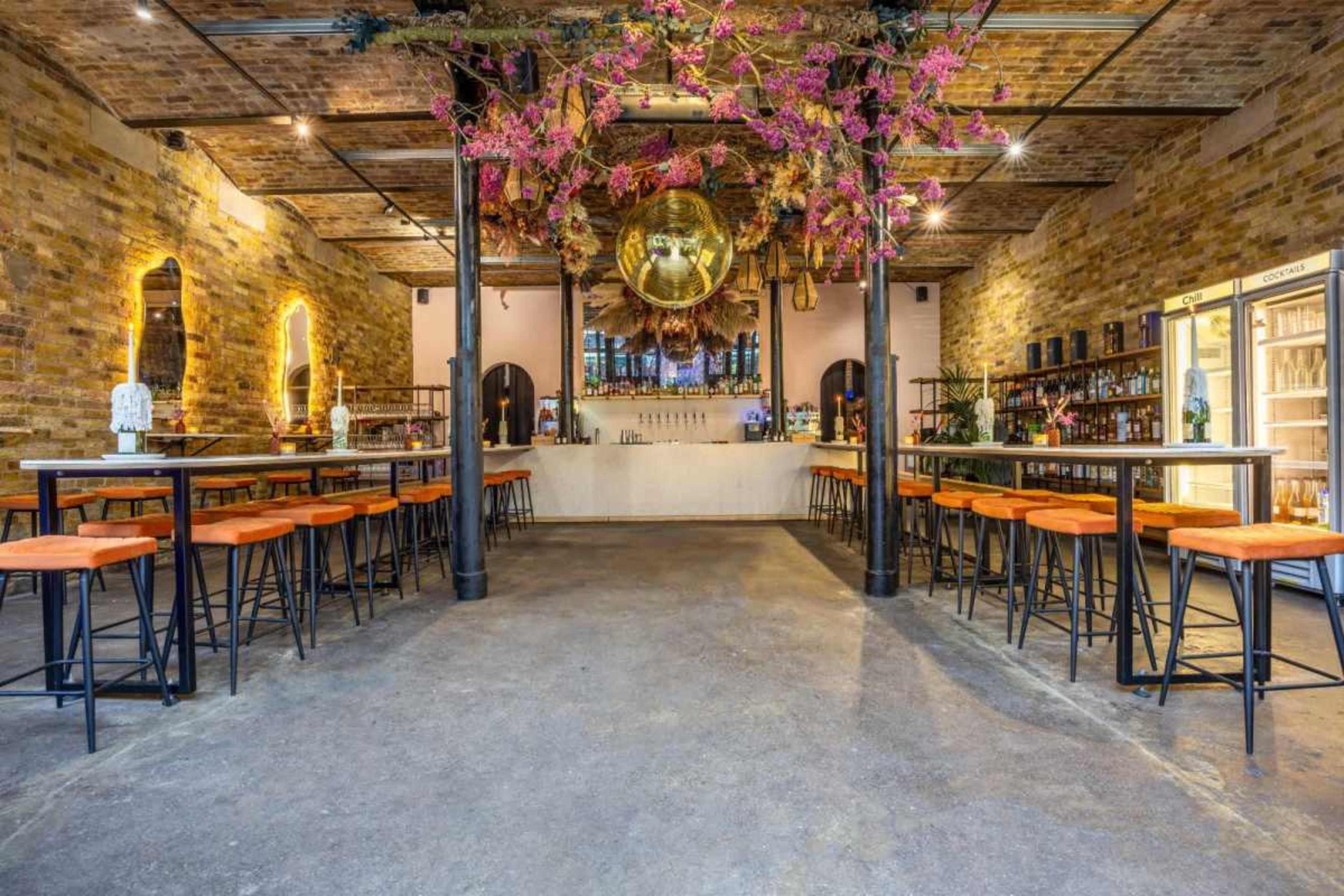 A spacious, rustic bar with a large round mirror hanging overhead and wooden walls adorned with floral decorations.