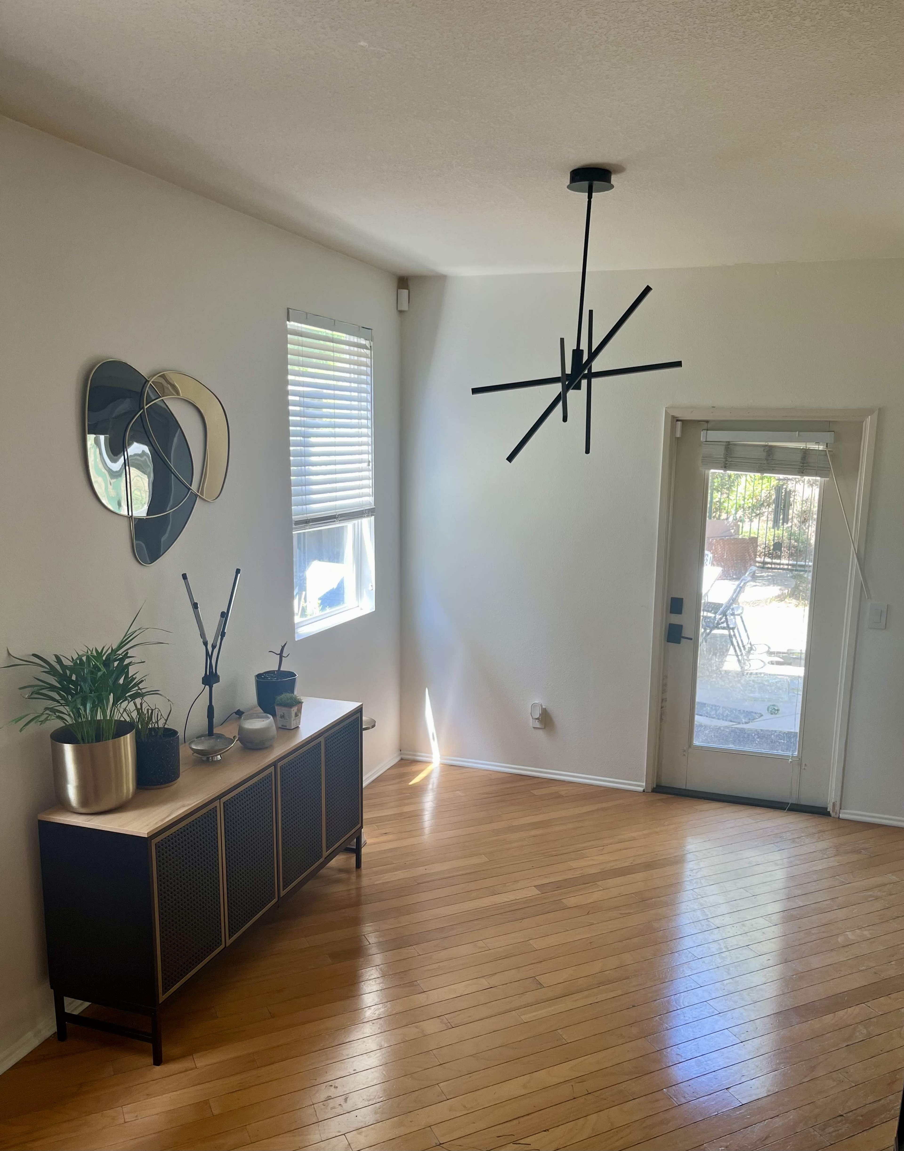 A well-lit open living space with a modern light fixture, a sideboard with decorative plants, and a sliding glass door leading to an outdoor area.