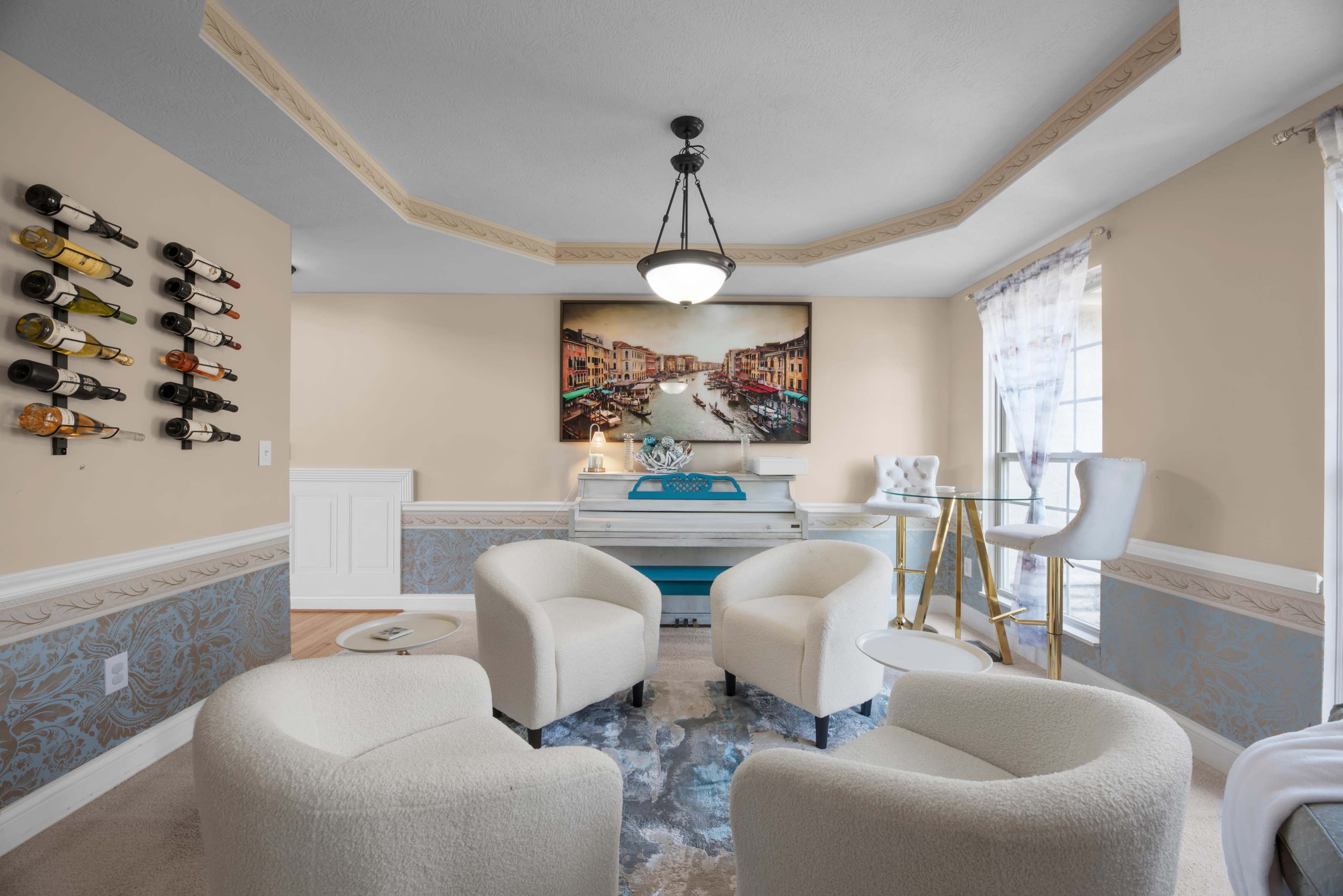 The image shows a cozy living room featuring four white upholstered chairs, a piano against the wall, and a large painting of a canal scene.