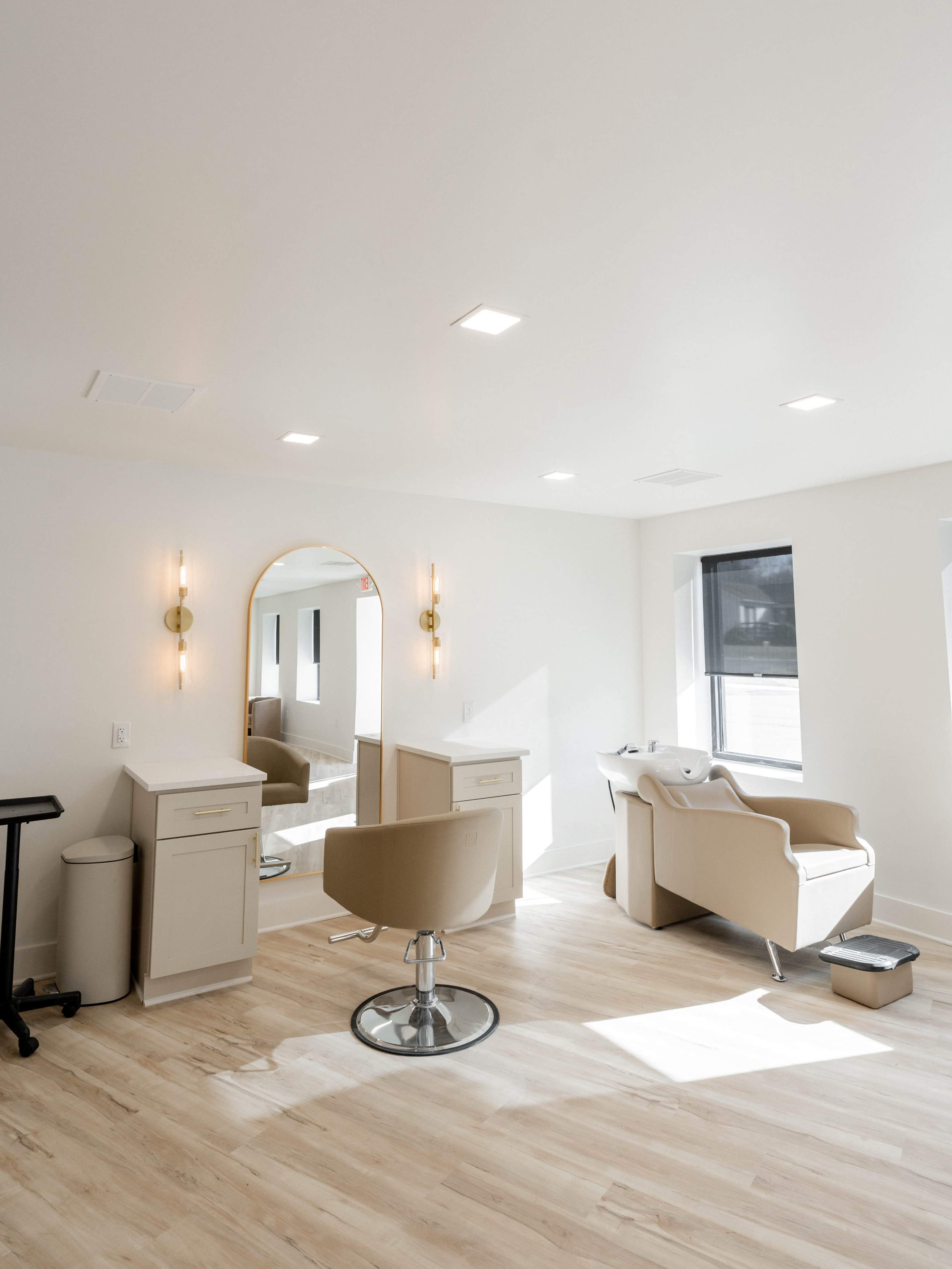 A bright, modern salon interior featuring a styling chair, a large mirror, and a beige futon.