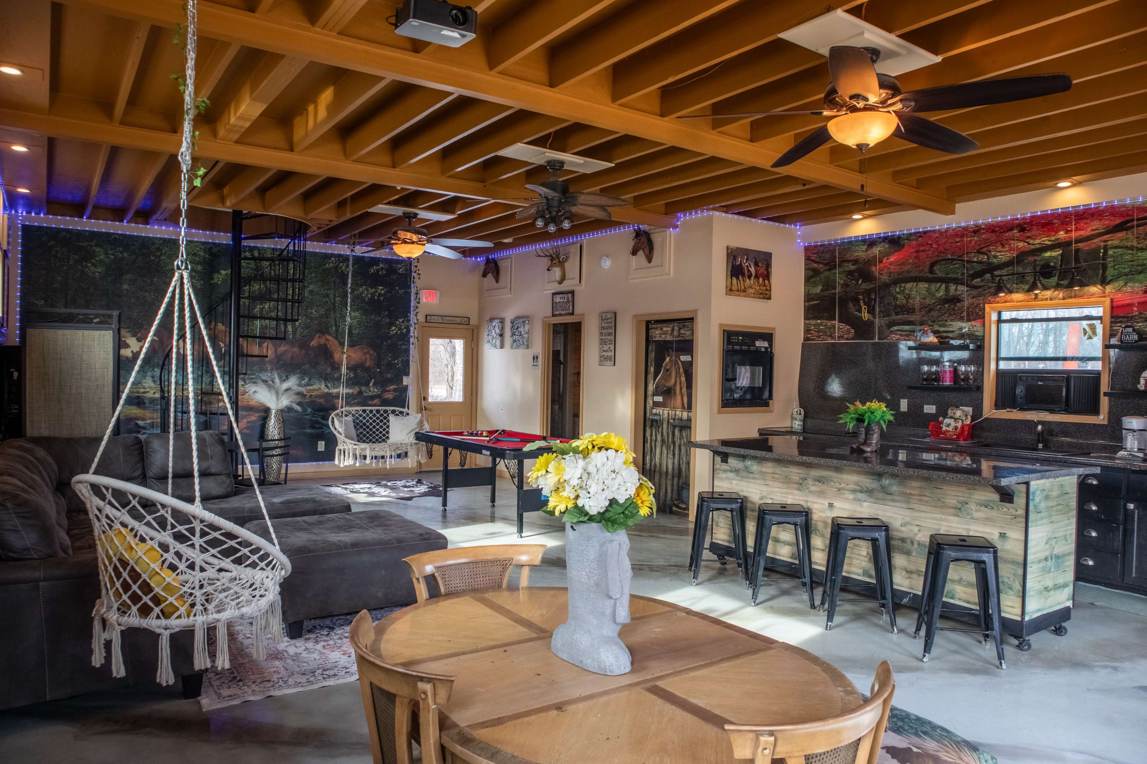 The image shows a cozy interior space featuring a living area with a large sectional sofa, a dining table, and a kitchen area, all decorated with rustic elements and ambient lighting.