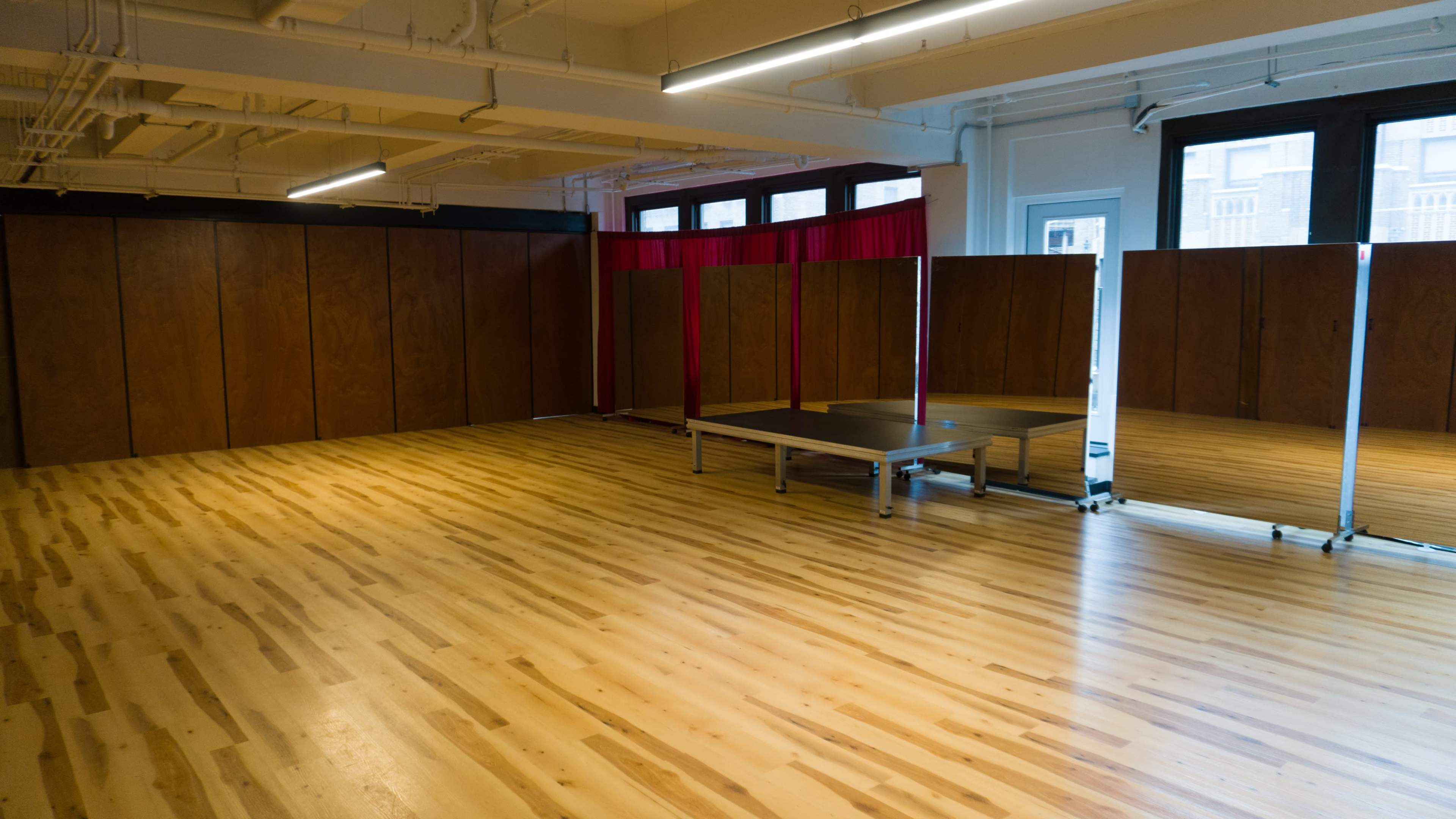 The image shows an empty room with wooden floors, equipped with dividers and a low platform against one wall.