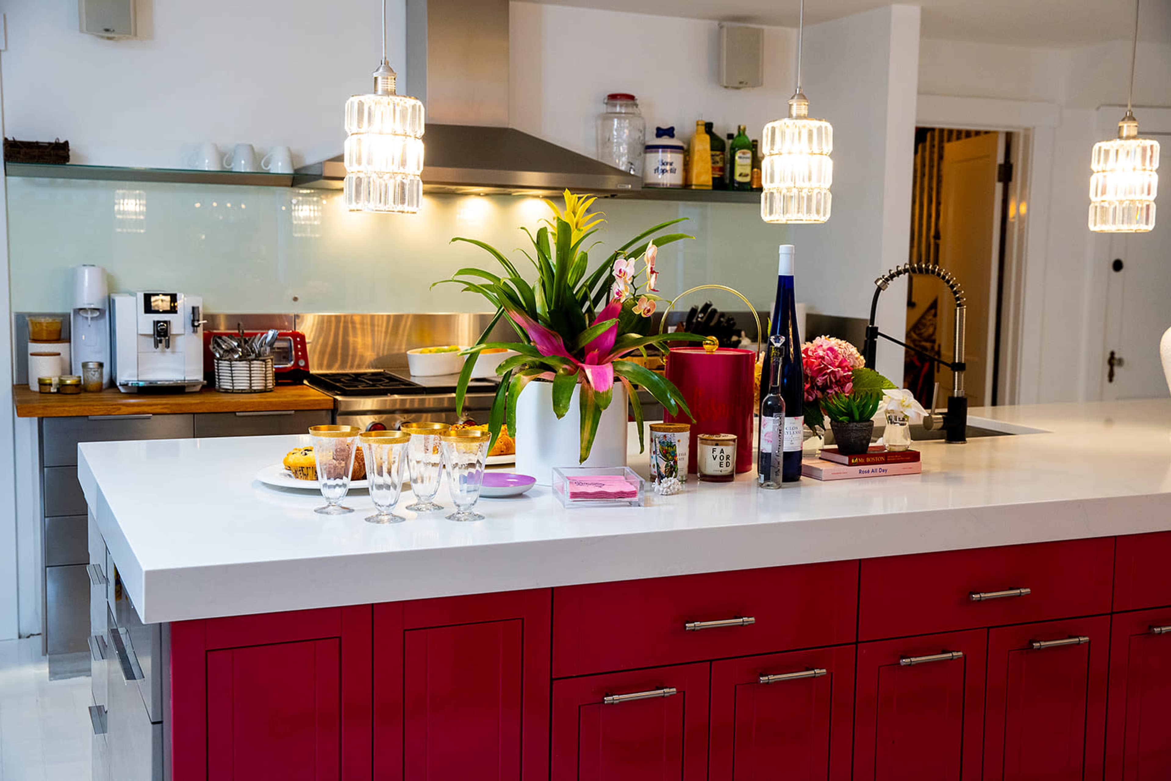 A modern kitchen with a bright red cabinetry, a white countertop, and various items arranged on the island, including snacks, drinks, and decorative plants.