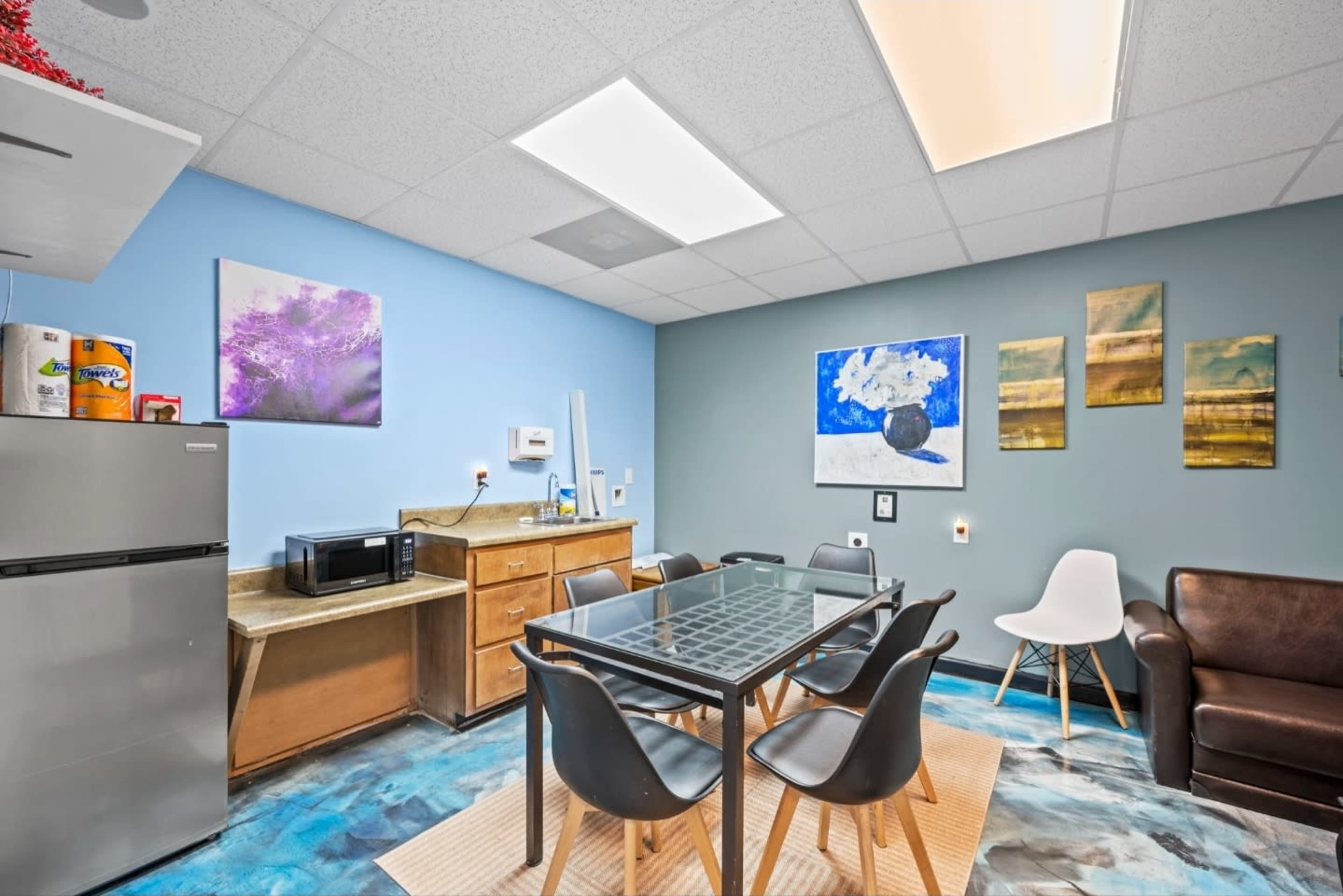 The image features a modern break room with a table and chairs, a refrigerator, a microwave, and colorful artwork on the walls.