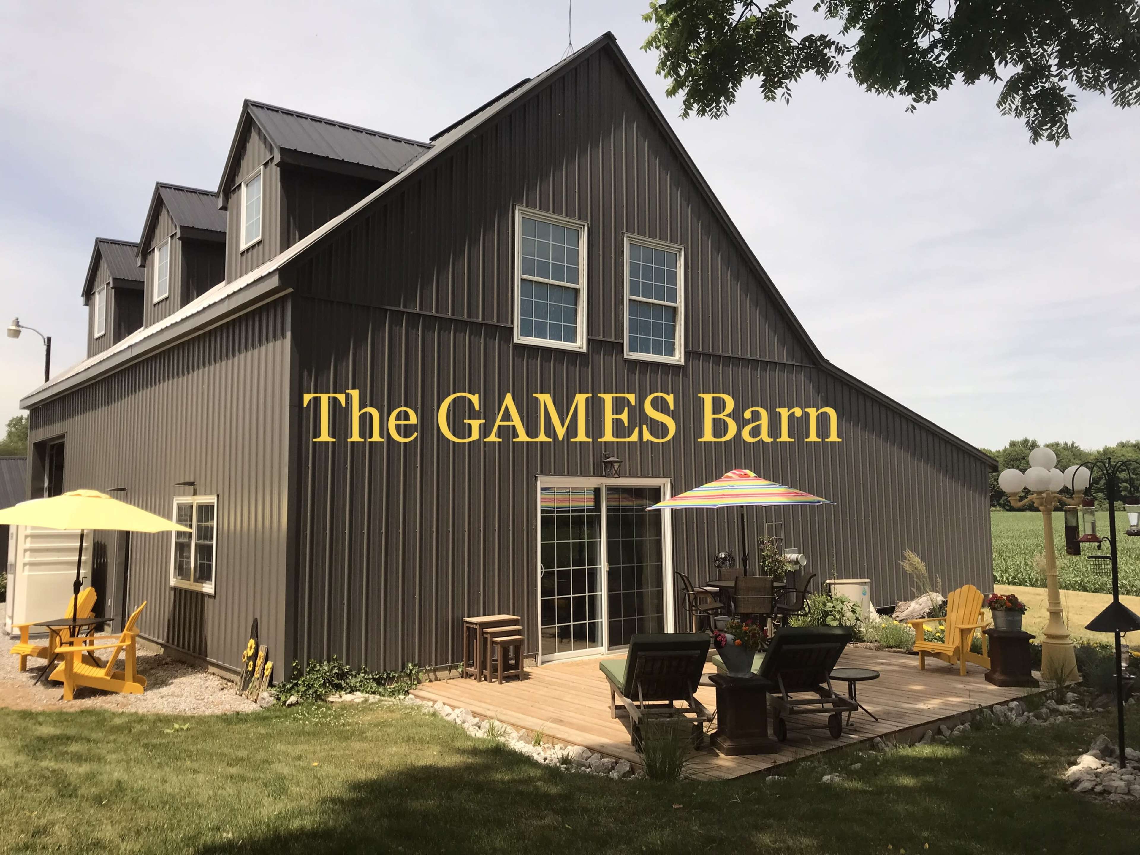 A large gray barn building with several windows and a deck featuring seating and patio umbrellas.