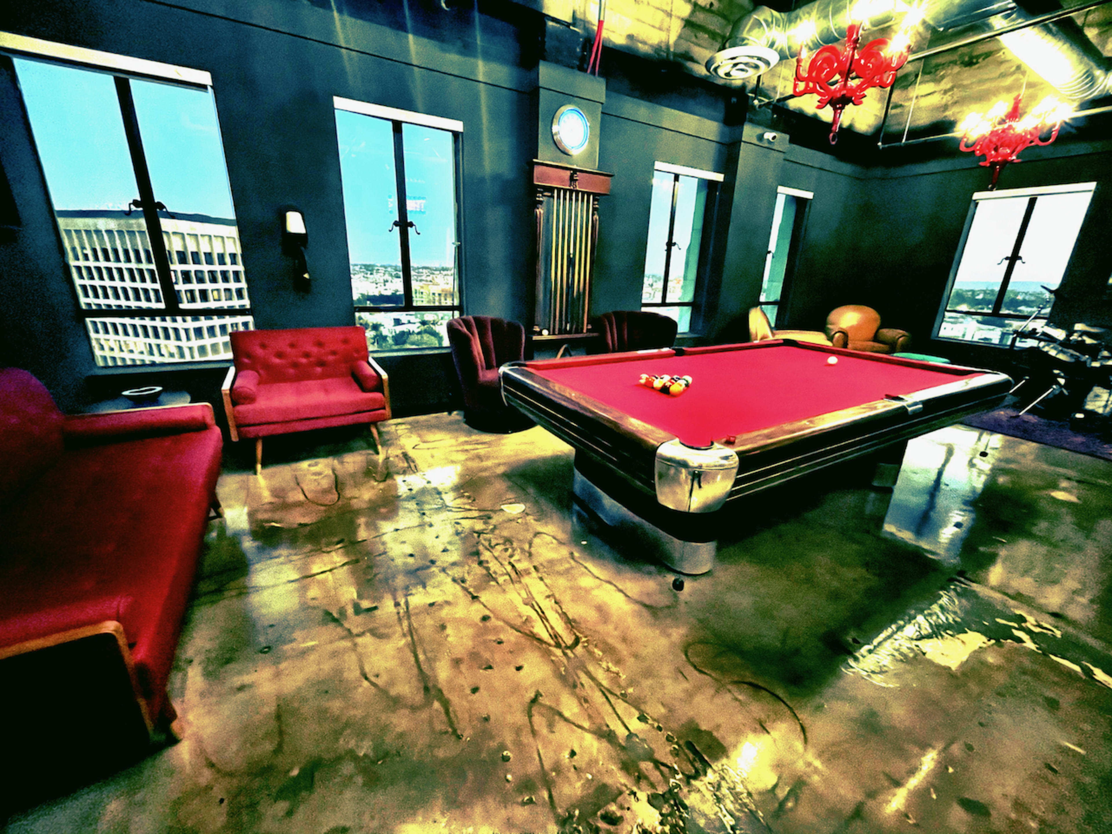The interior features a billiard table surrounded by red sofas and large windows, with city views visible in the background.