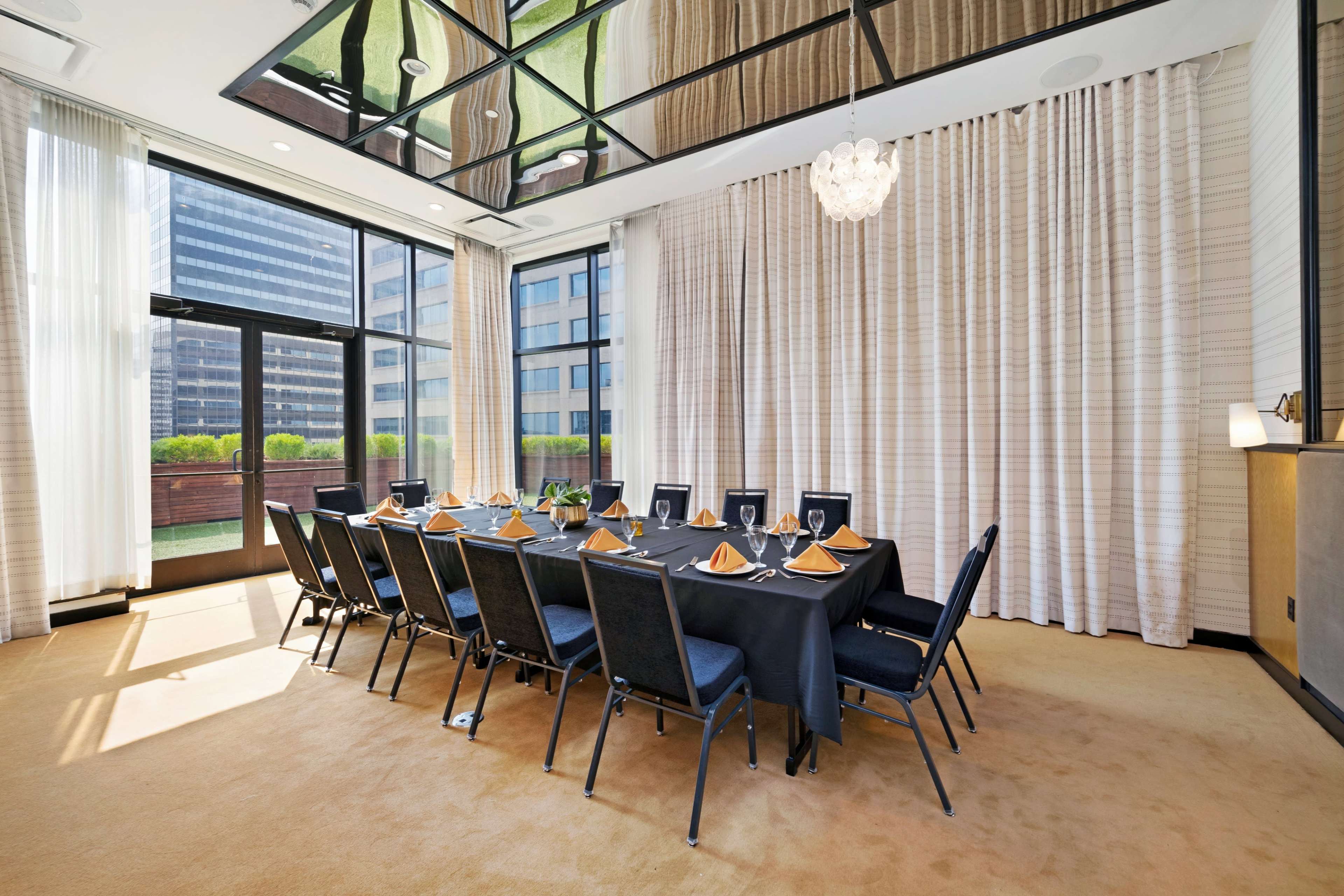 A conference room with a long table set for dining, surrounded by large windows and floor-to-ceiling curtains.
