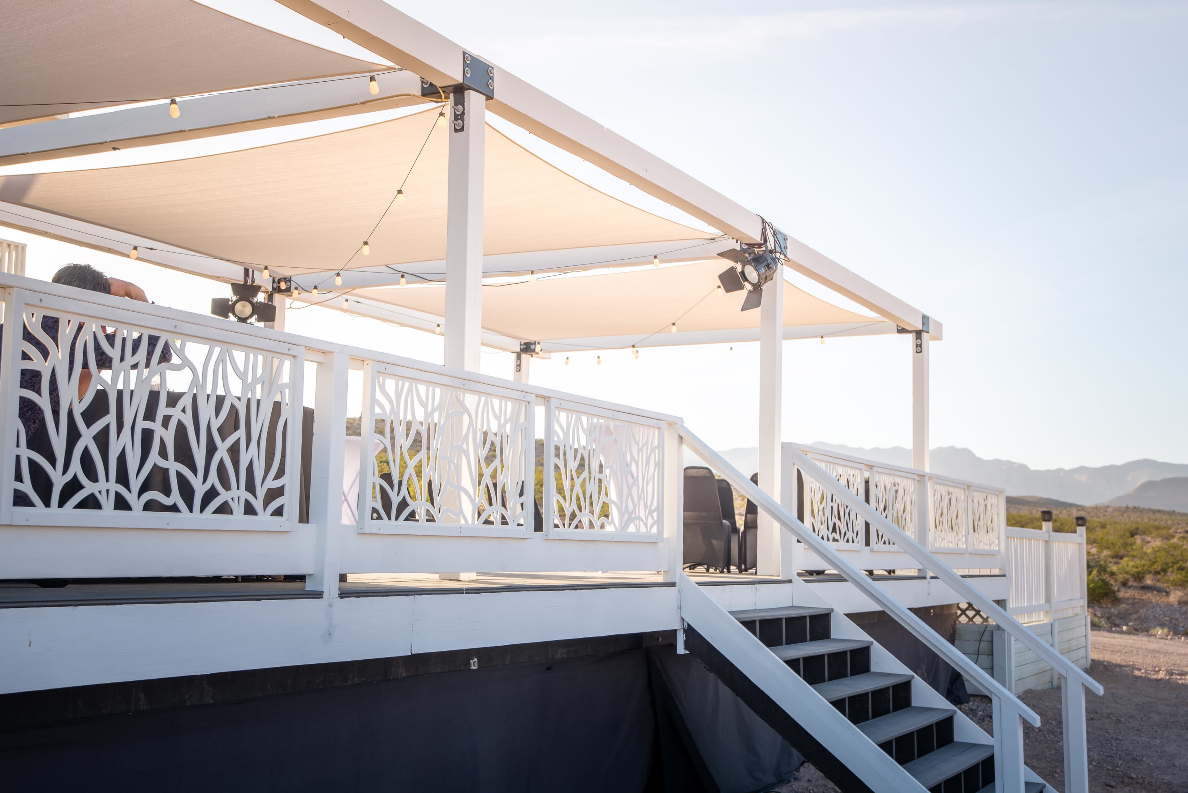 A raised deck with a white railing and stairs, set against a backdrop of mountains and a clear sky.