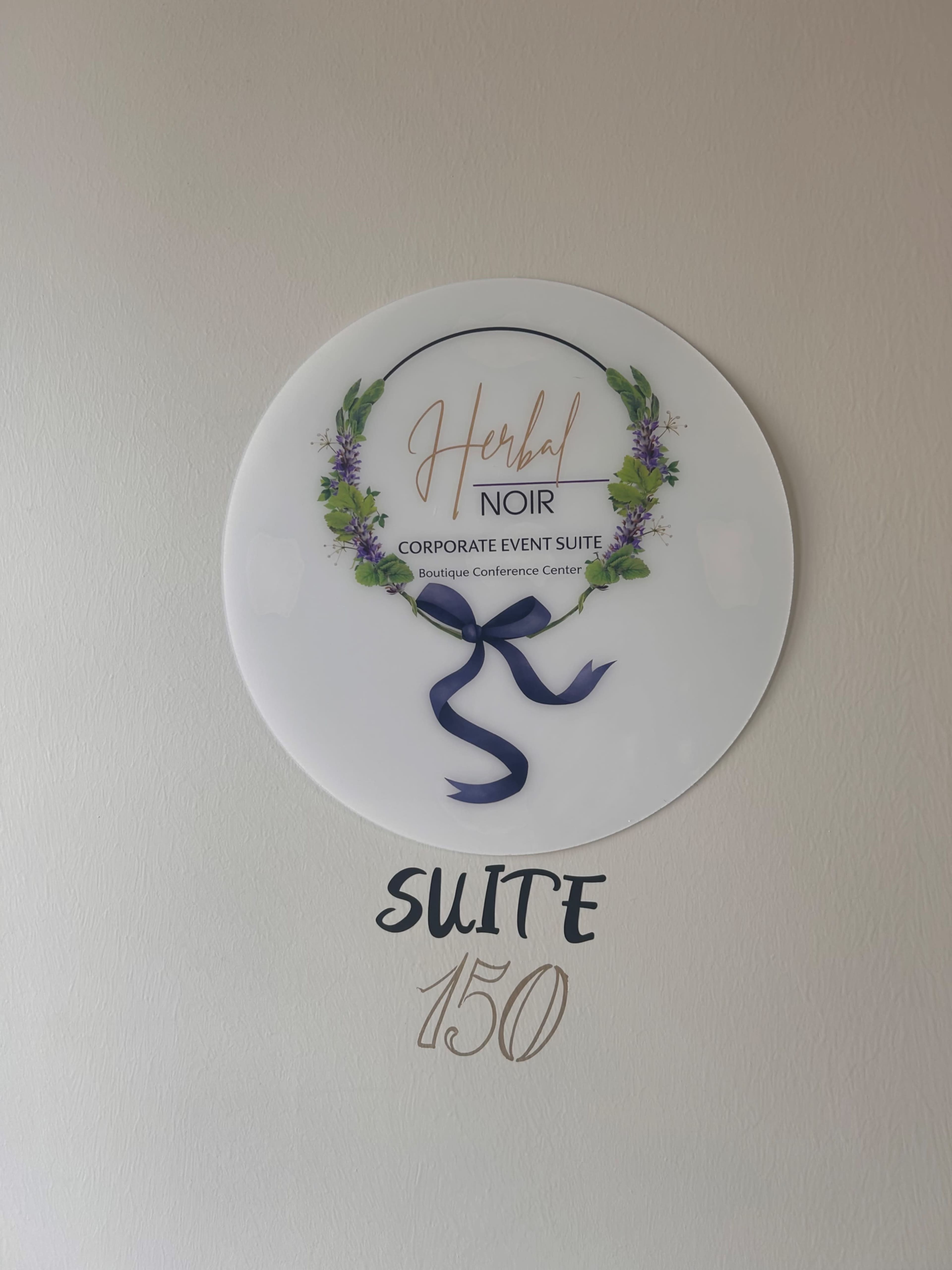 The image shows a sign for "Herbal Noir" Corporate Event Suite, located in Suite 150 of a Boutique Conference Center.