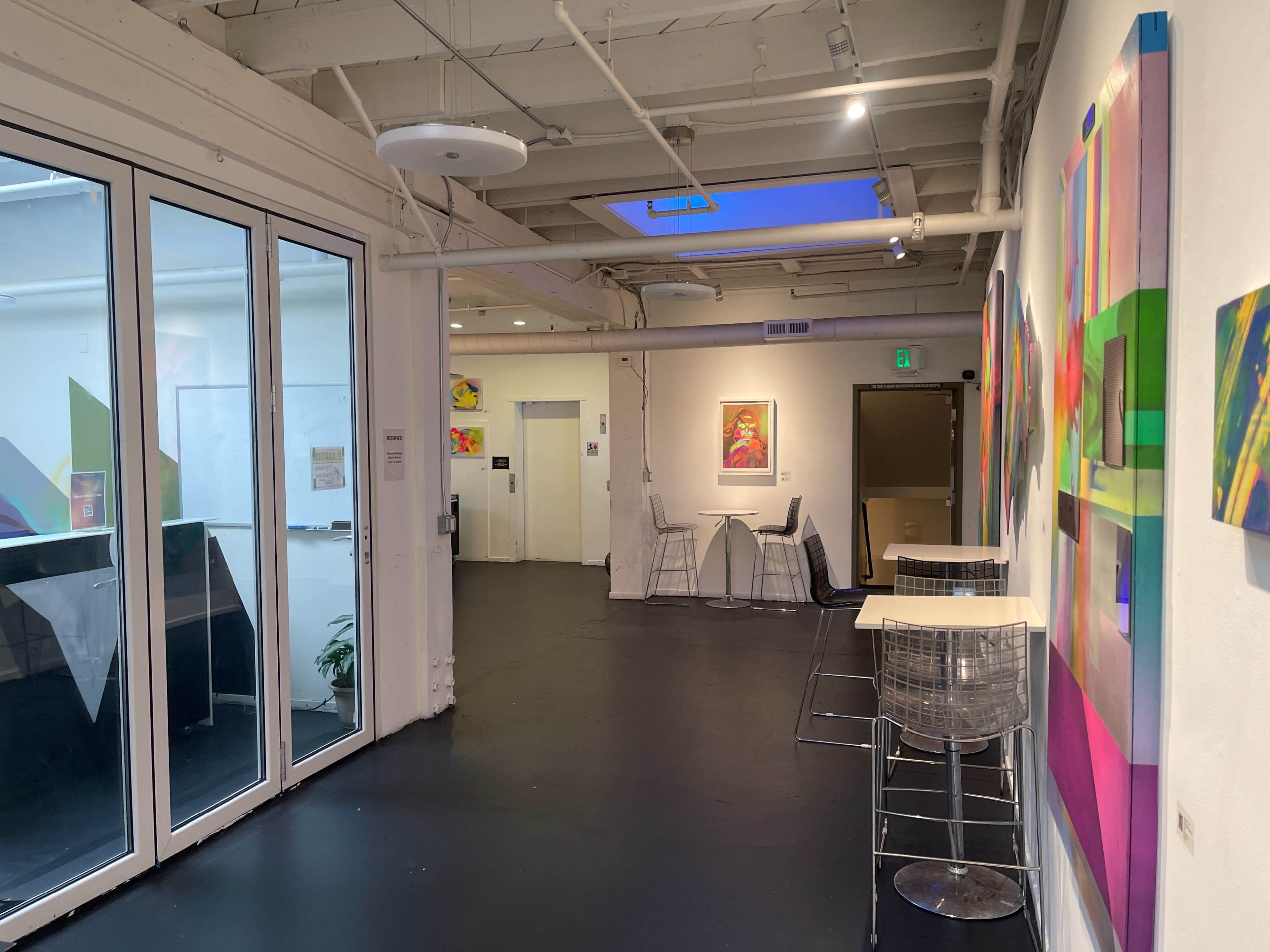 An art gallery with modern decor, featuring colorful abstract paintings on the walls and a small seating area.
