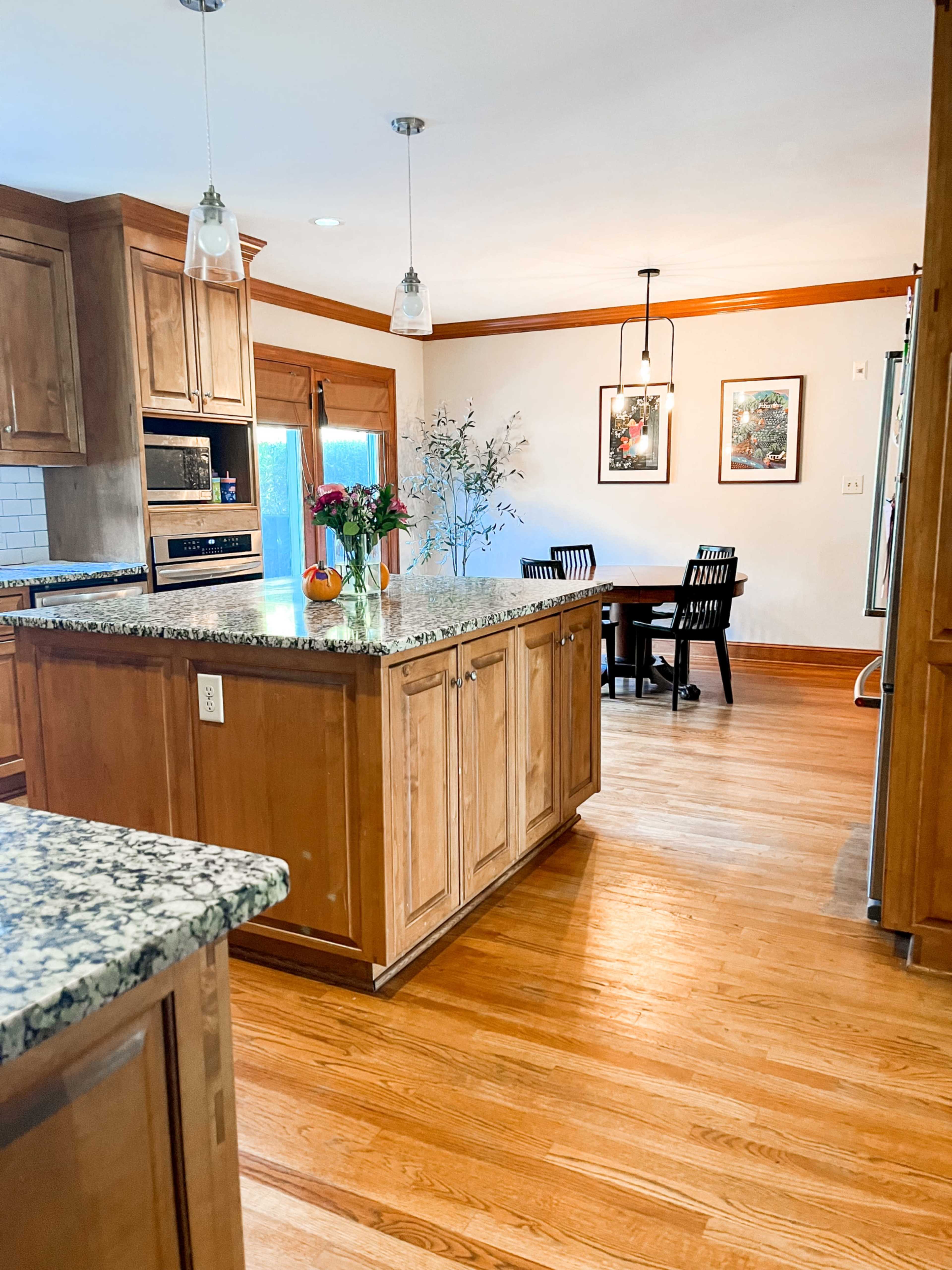 A spacious kitchen with wooden cabinets, a granite island, and a dining area featuring a round table and four black chairs.