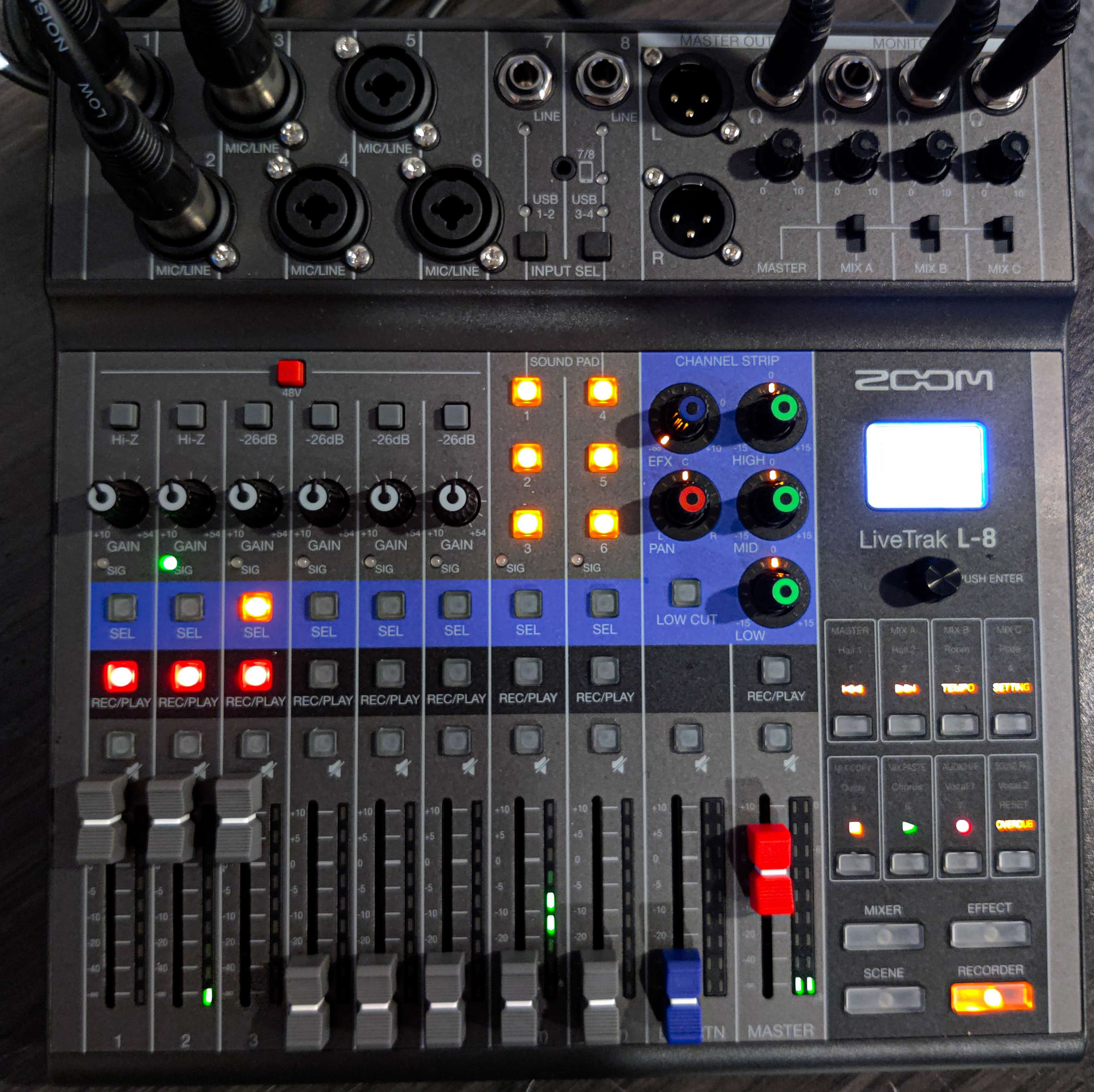 A Zoom LiveTrak L-8 audio mixer with various input channels, knobs, and LED indicators illuminated.