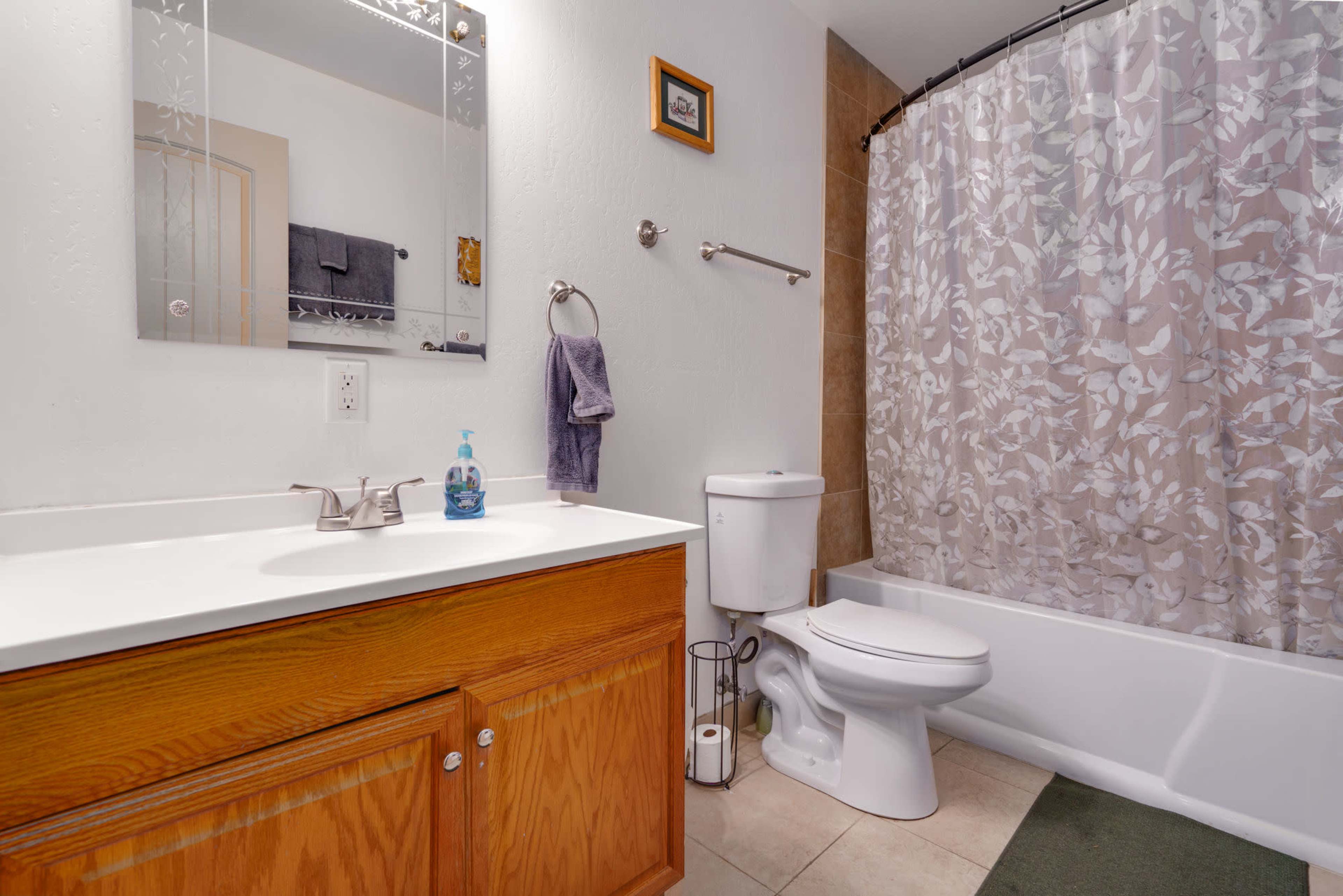 A bathroom features a wooden vanity with a sink, a toilet, and a tub with a floral shower curtain.